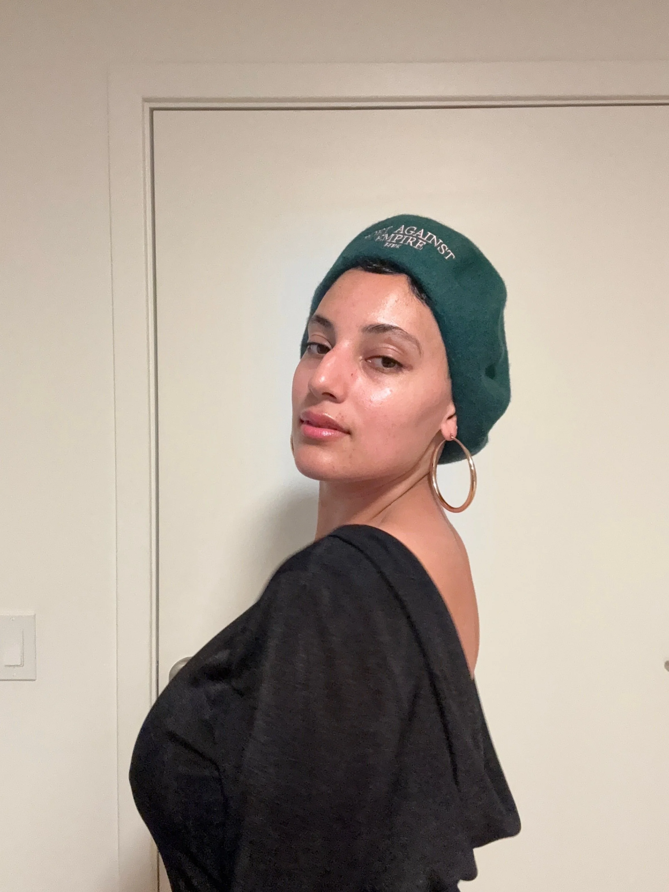 Siobhan poses with green beret against white door.