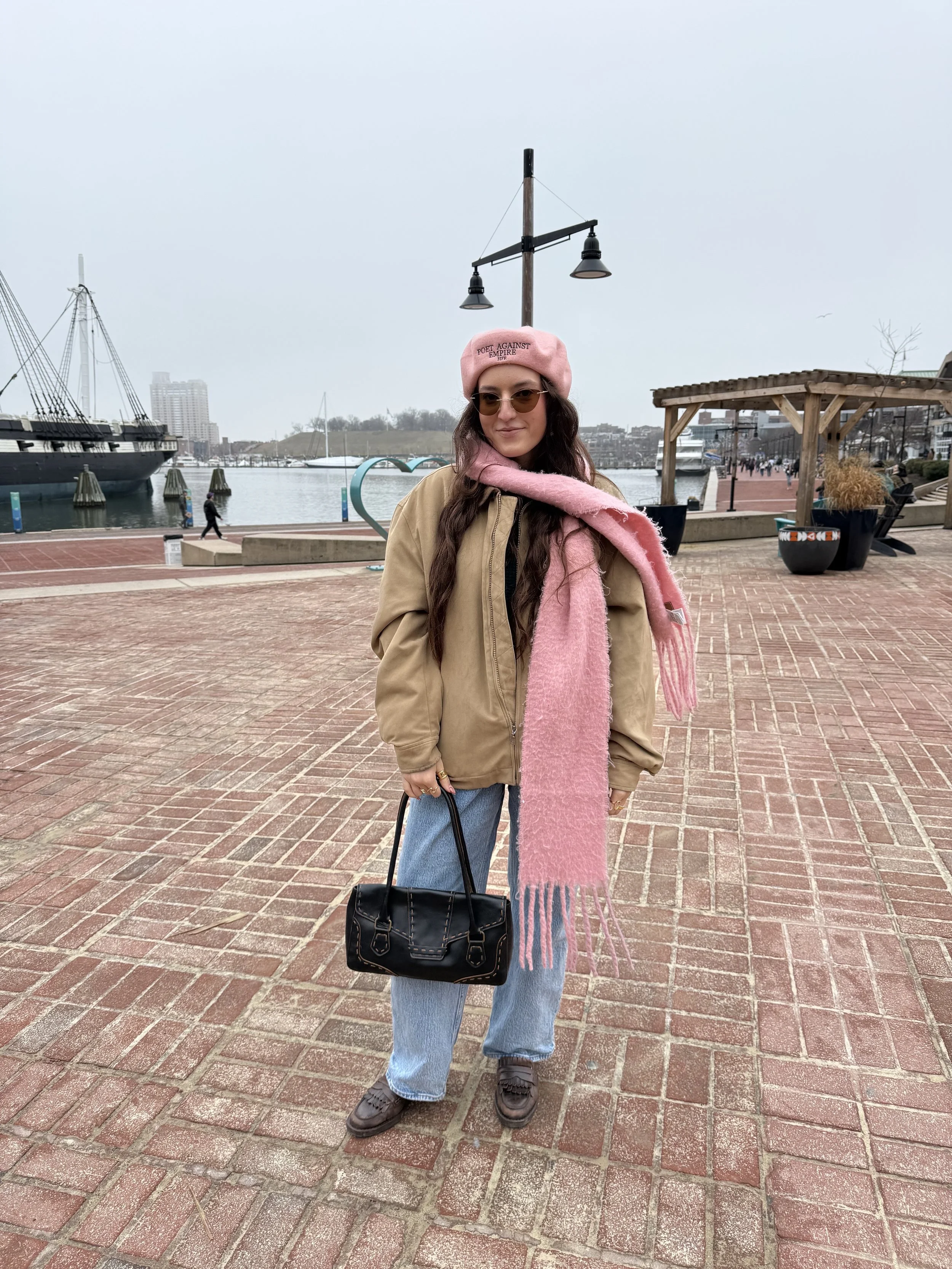 Hana poses with pink beret and pink scarf in front of Baltimore Harbor.