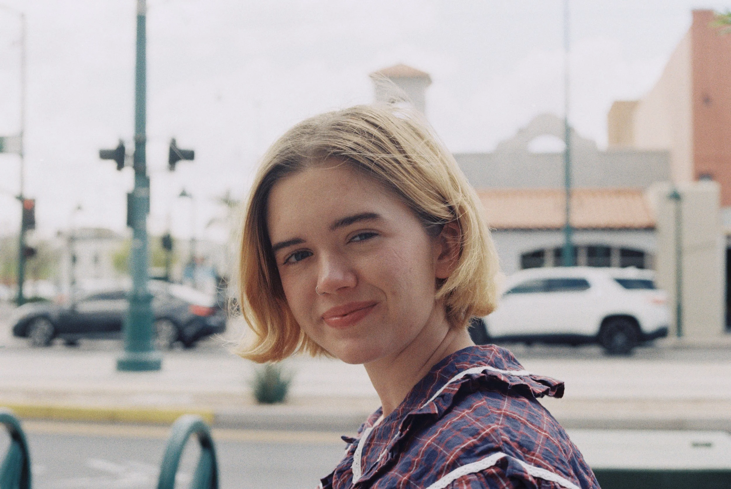 Headshot of Audrey turning towards the camera with a closed-mouth smile and standing outside in front of a parking lot.