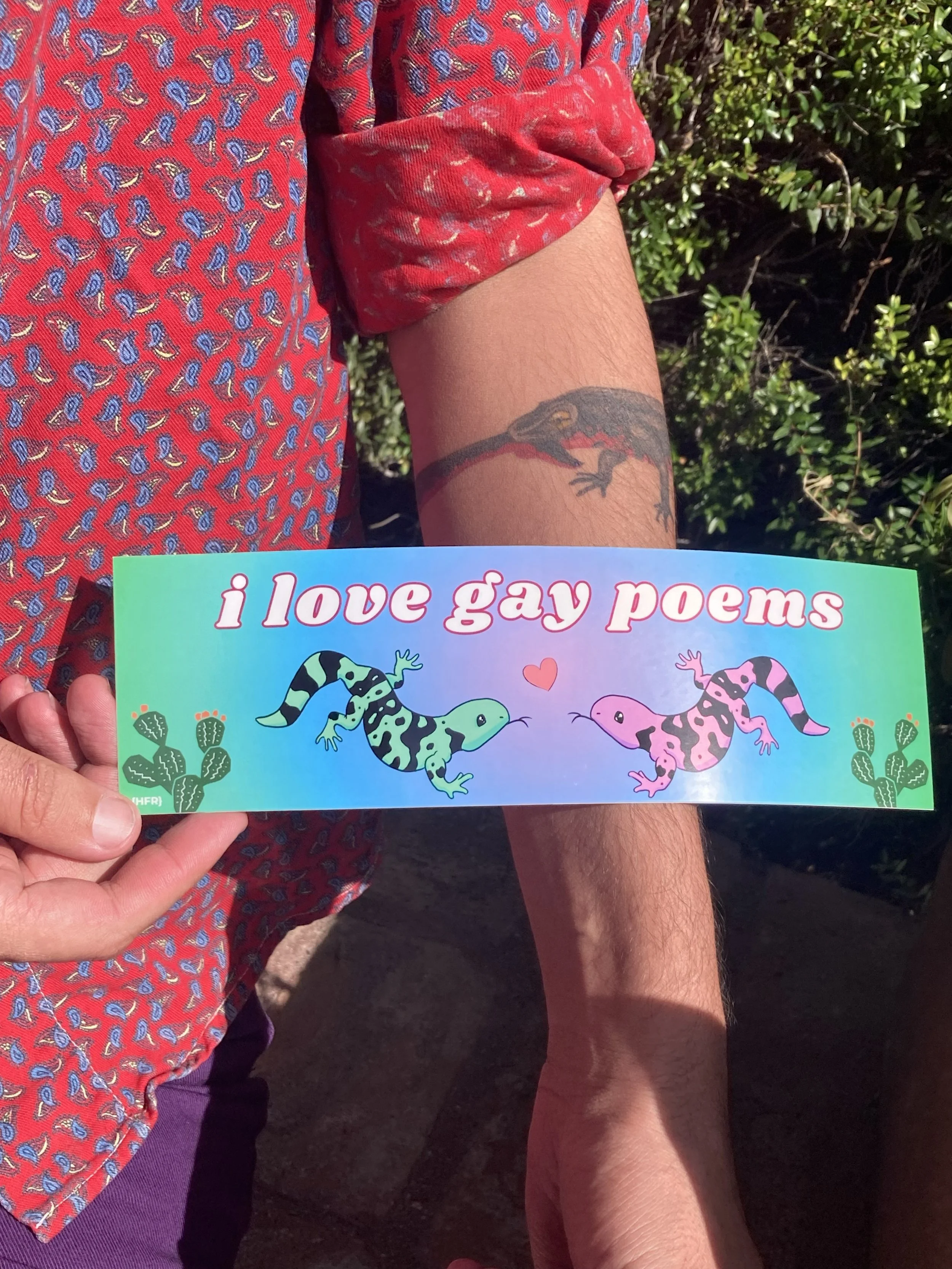 I love gay poems sticker held against person's lizard tattoo