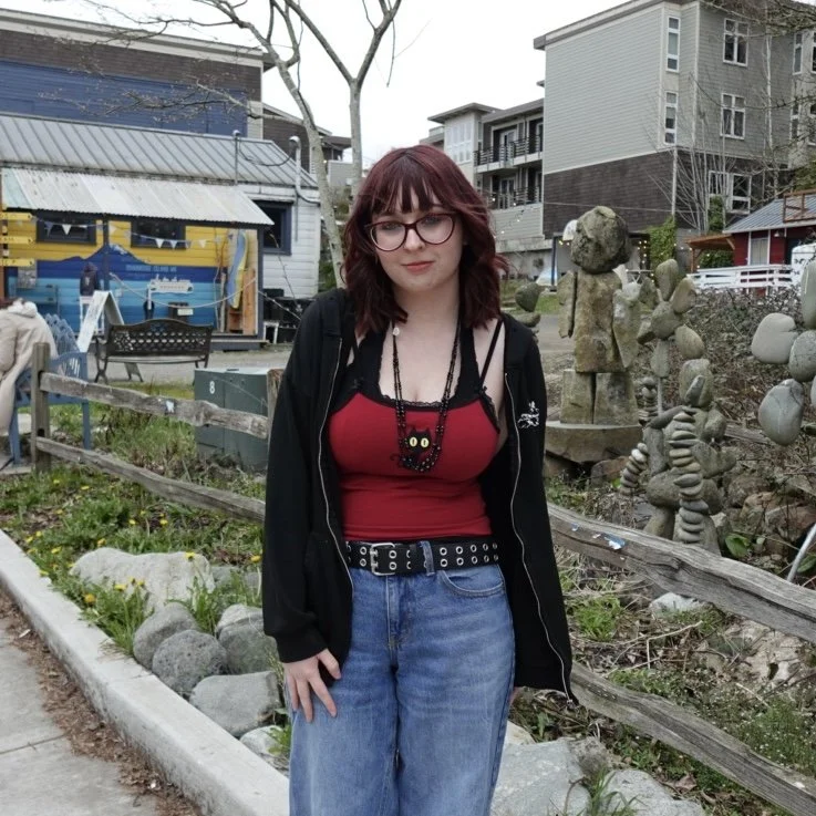 Eva in red top and black sweater stands outside and looks at camera.