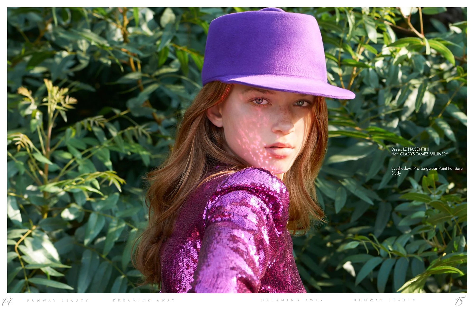 A young model with red hair wearing a purple sequined top and a purple hat, standing outdoors in front of green foliage, shot by photographer Daniella Hehmann