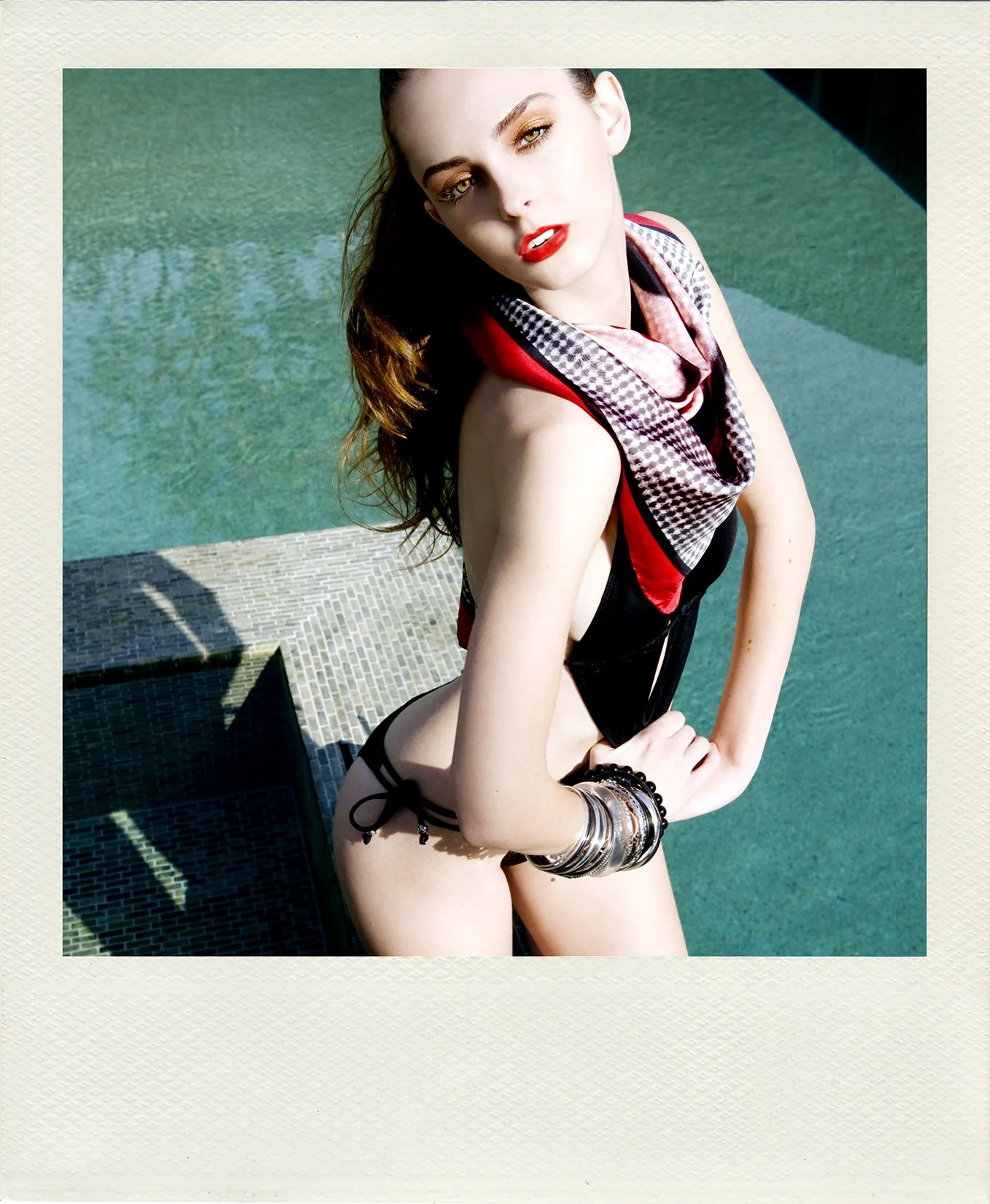 Photography by Daniella Hehmann: A Polaroid-style fashion portrait of a model in black swimwear and a patterned neck scarf by a pool.