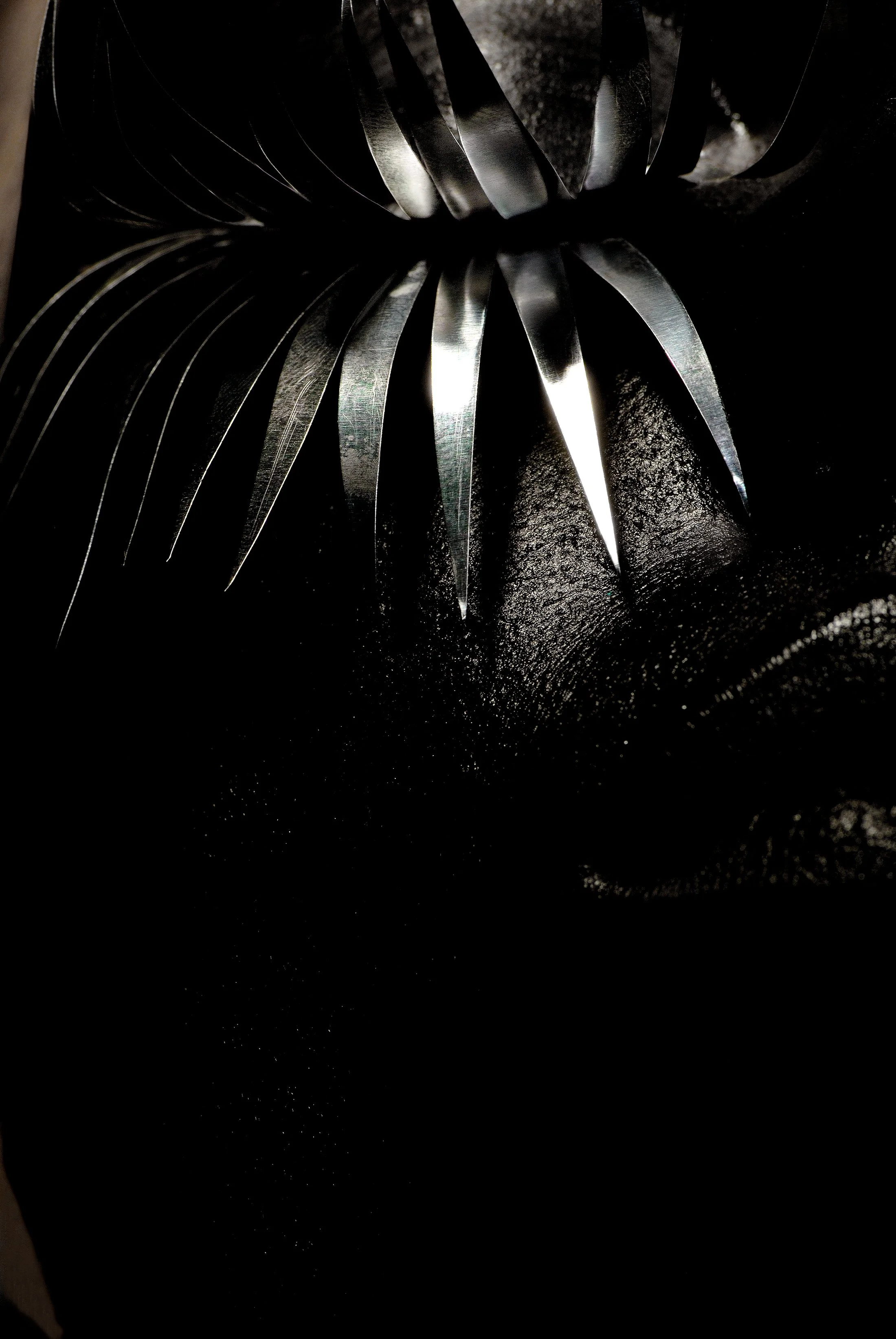 Close-up of metallic object with curved, sharp-edged blades or pieces, reflecting light against dark background.