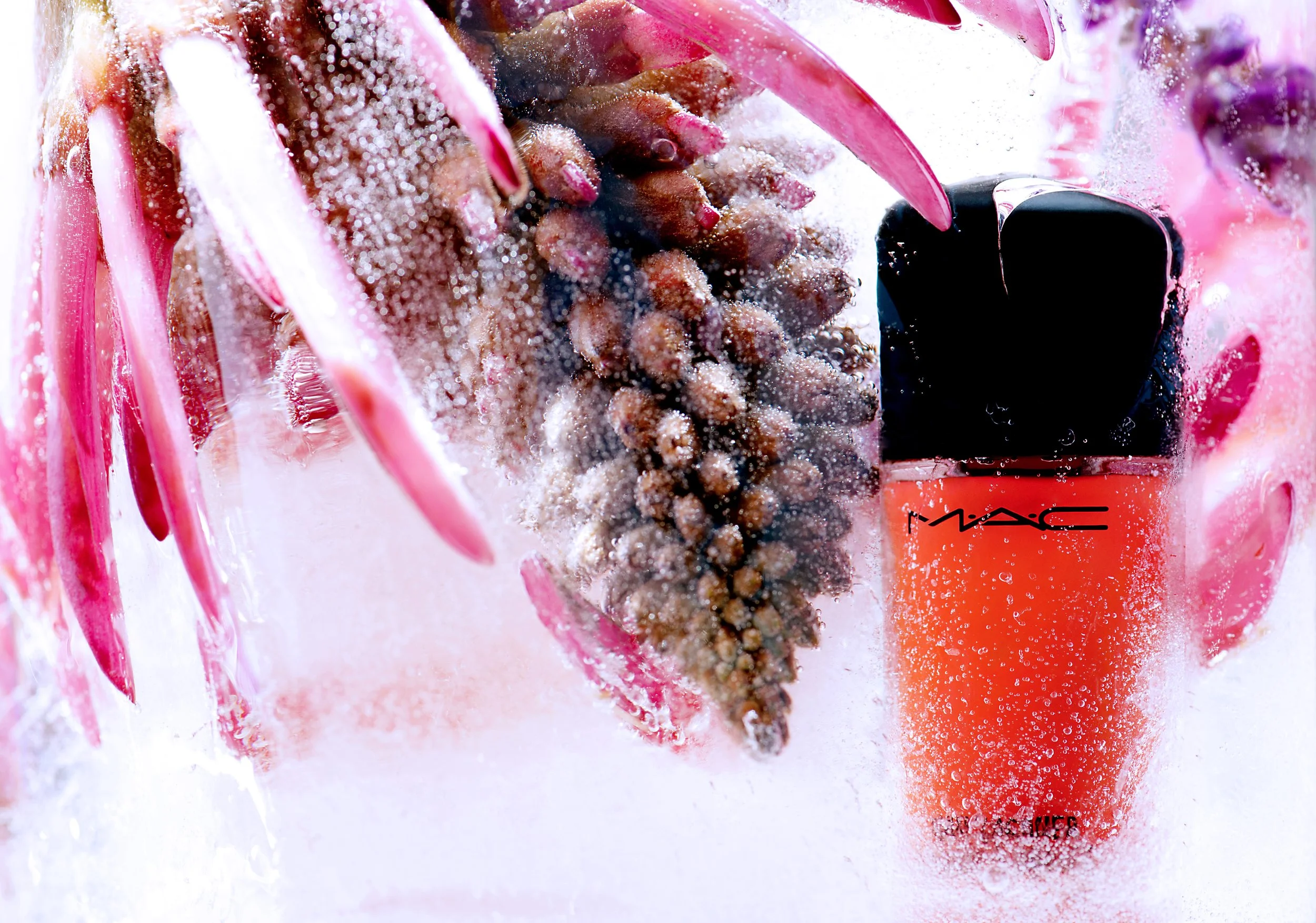 Close-up of a pink pineapple and a bottle of MAC Cosmetics liquid lipstick submerged in ice and snow, with bubbles and frost around them.
