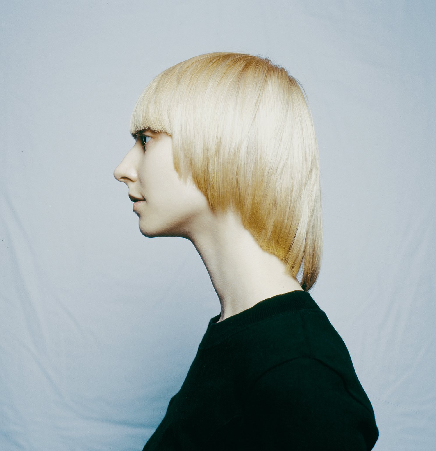 Precision hair photography by Los Angeles and Munich photographer Daniella Hehmann featuring a Vidal Sassoon model. A side-profile shot of a blonde model with a sharp, geometric bob haircut and blunt bangs. Minimalist studio lighting and a clean back