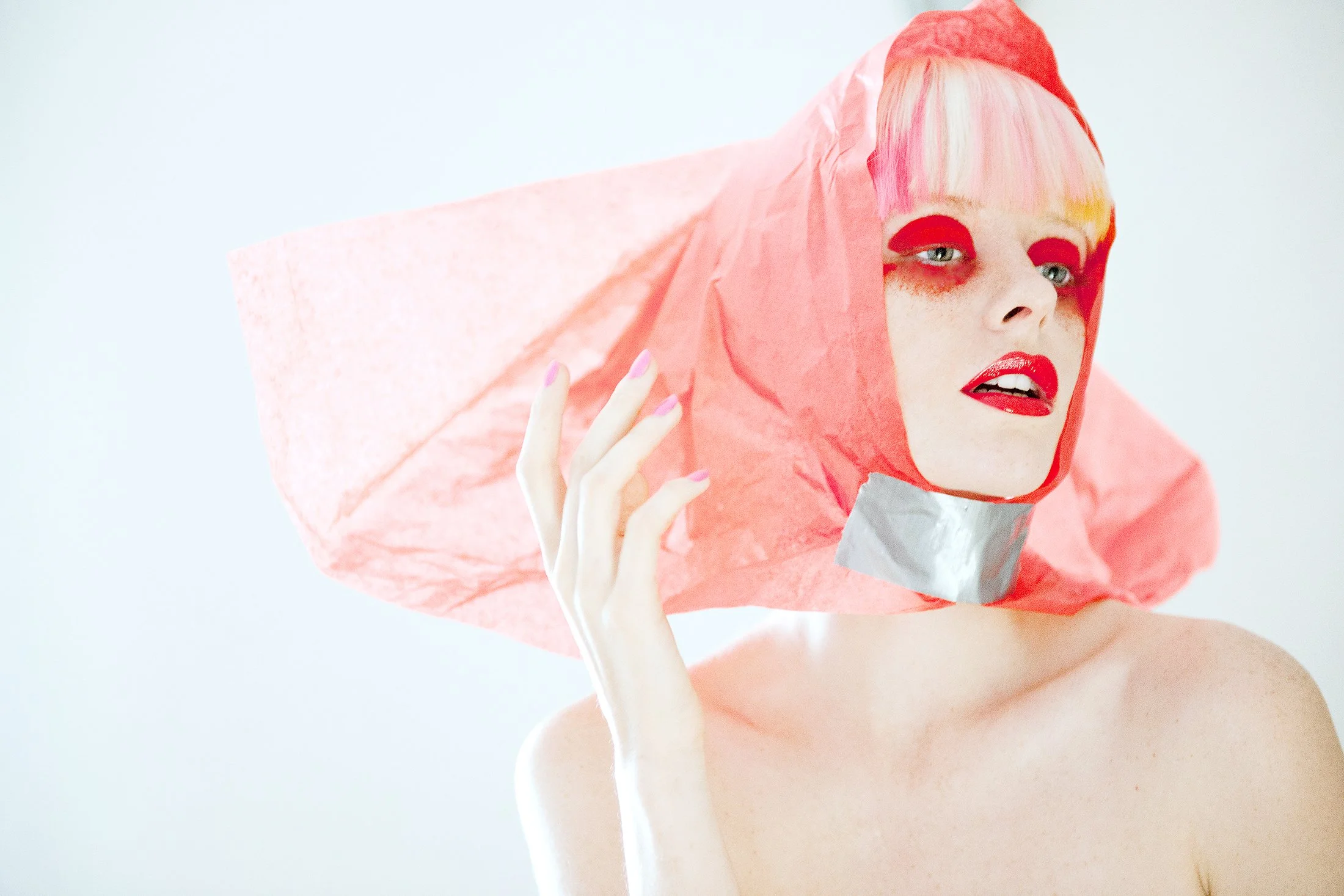 Conceptual beauty portrait by expert photographer Daniella Hehmann featuring bold red lips styled with a structural red paper hood and silver industrial tape under bright beauty lighting. L.A. based.
