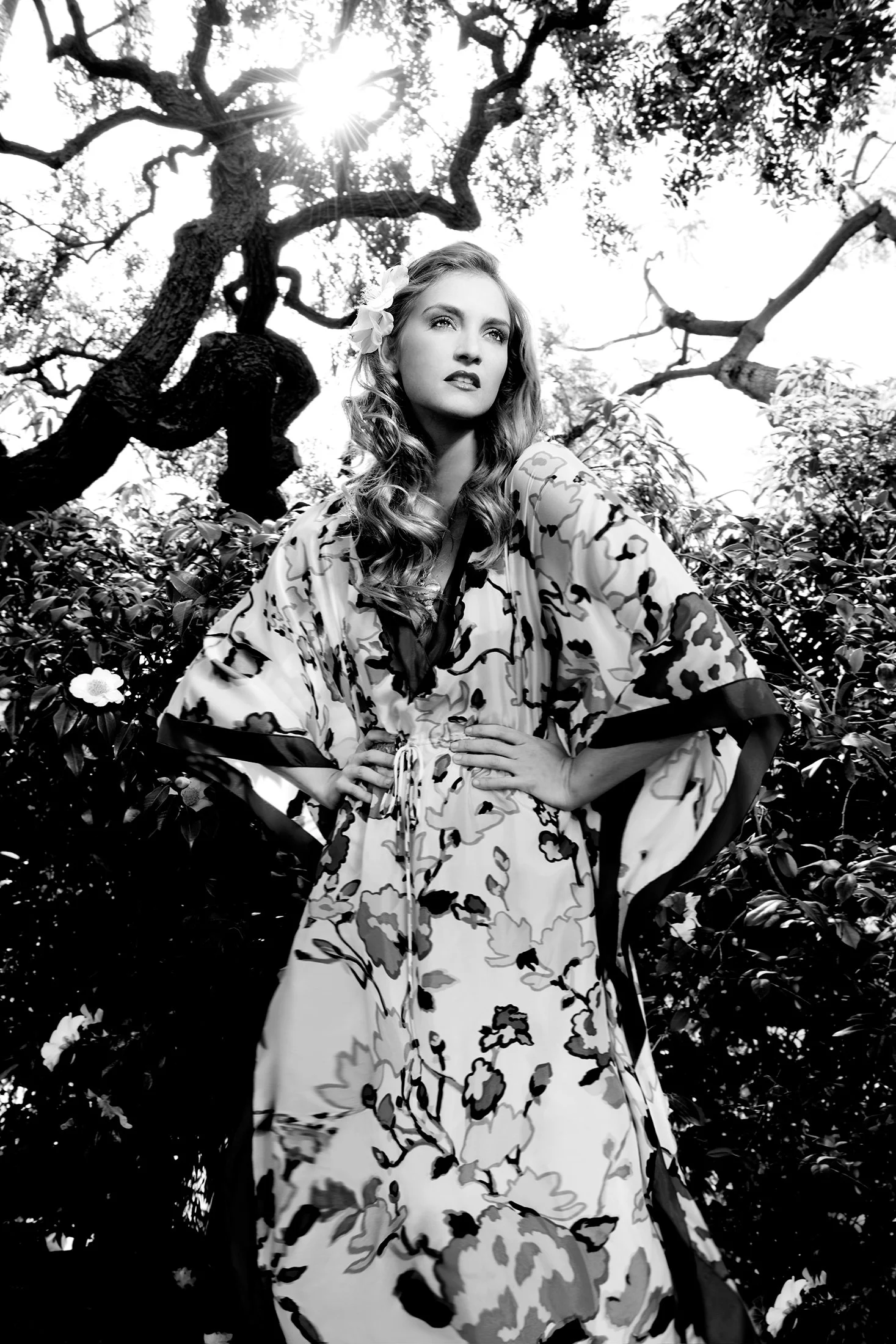 Photography by Daniella Hehmann: A black and white artistic portrait of a model in a floral patterned robe amidst trees.