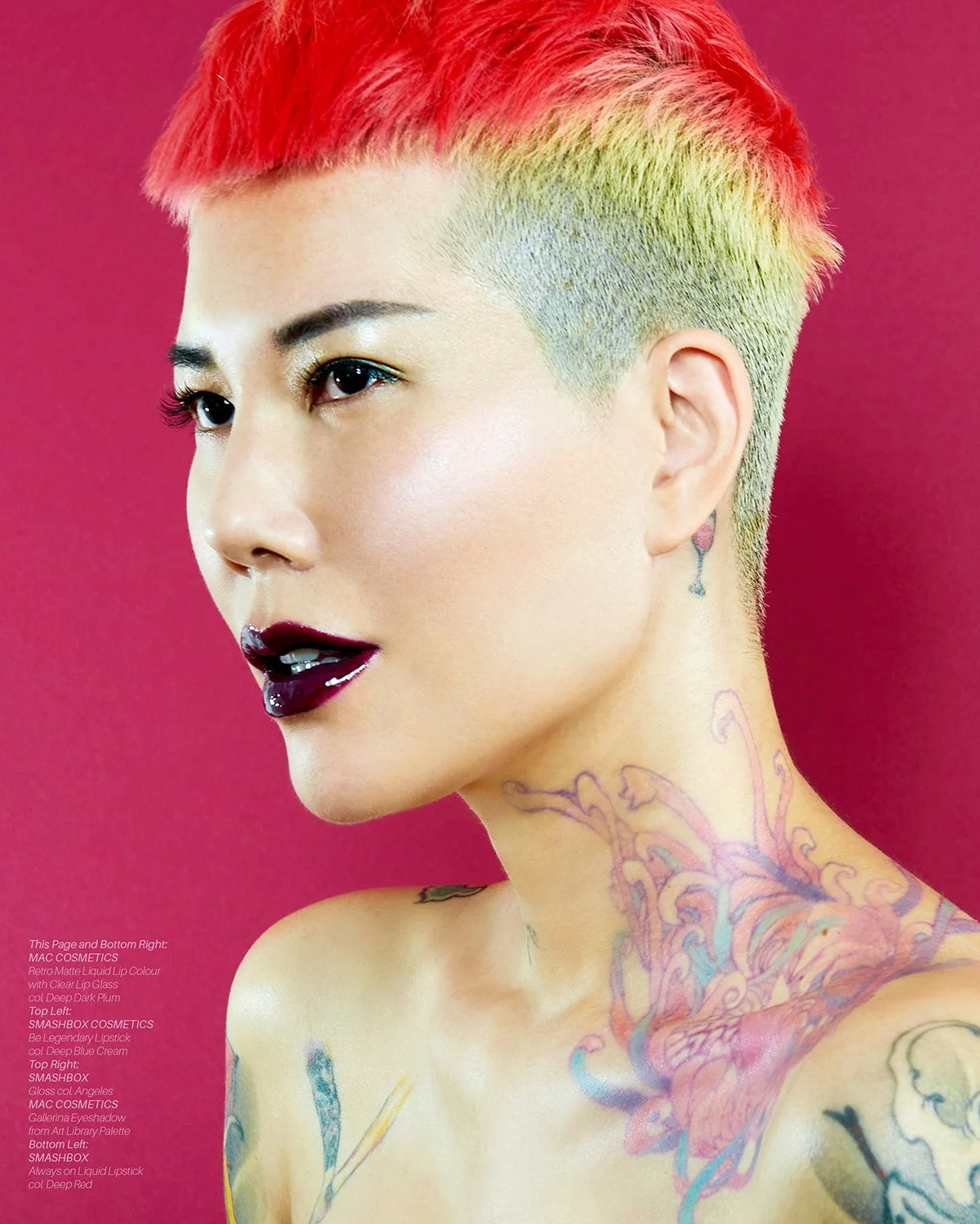 Beauty photography by Daniella Hehmann: Close-up of a woman with short, multicolored hairstyle with red on top and blonde sides, dark lipstick, and multiple tattoos on her neck and shoulders, set against a solid pink background.