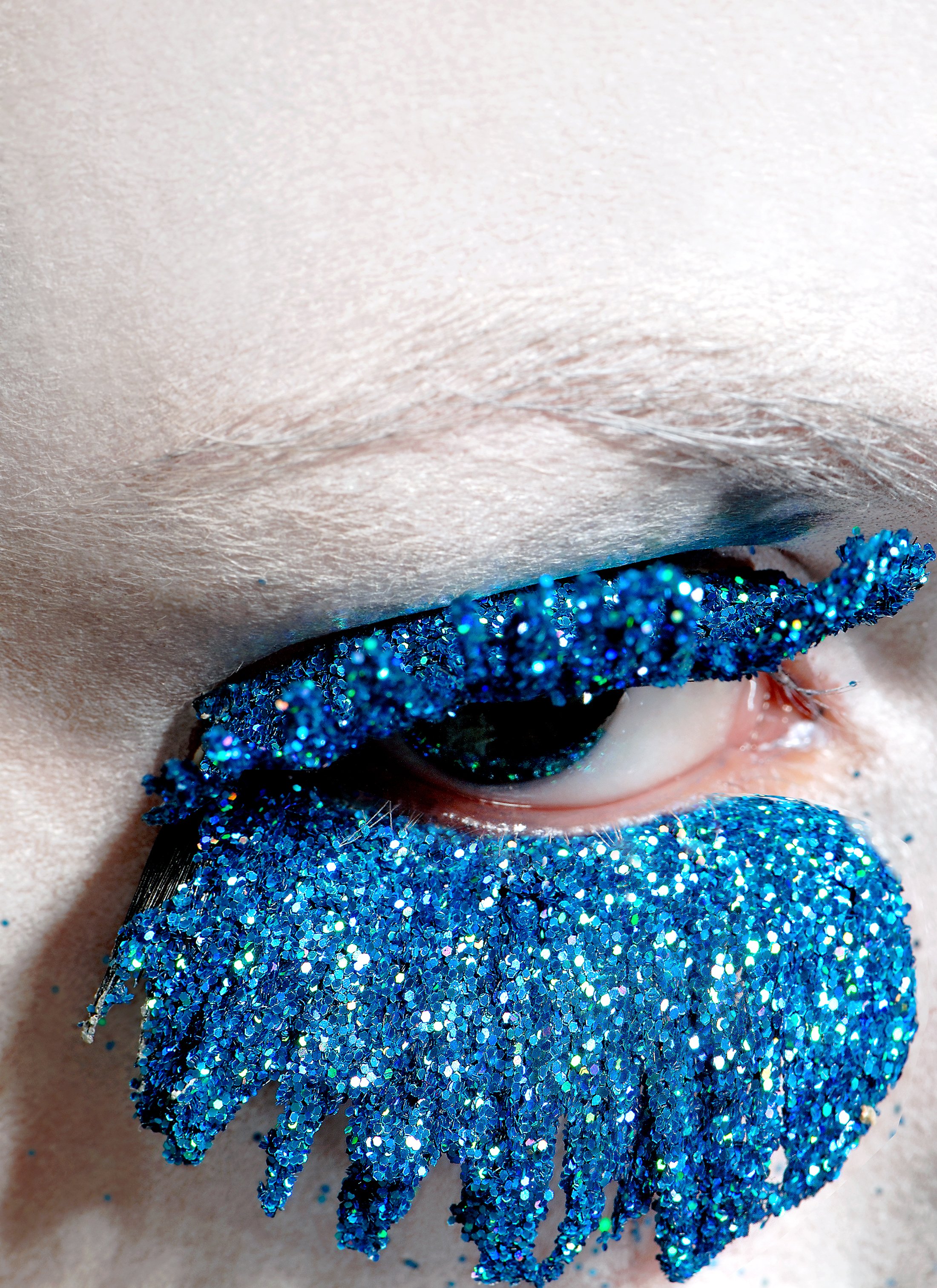 Avant-garde macro beauty shot by Daniella Hehmann featuring custom made heavy cobalt blue glitter faux eyelashes. This fine art personal project uses sharp studio lighting to capture the brilliant sparkle and texture of the glitter, demonstrating exp