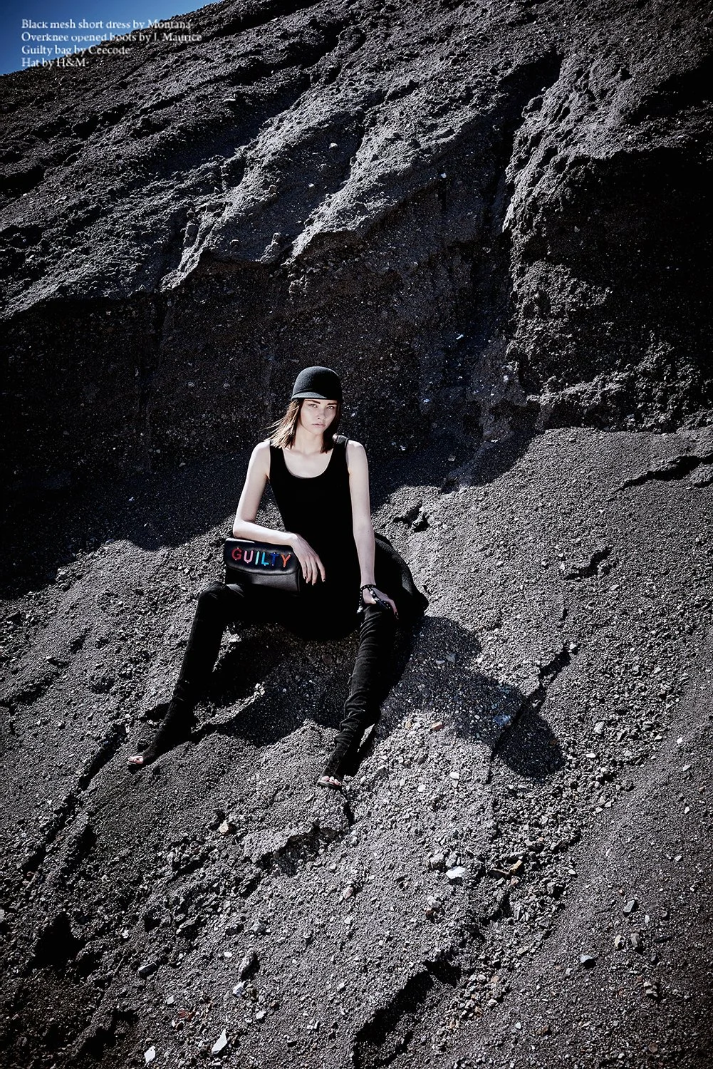 Cinematic editorial photography by Daniella Hehmann Photography for the 'Outer Rim' spread in L.A. A model in an edgy all-black outfit sits on a steep, futuristic dark gravel slope, emphasizing a desolate, otherworldly atmosphere. She is wearing a bl