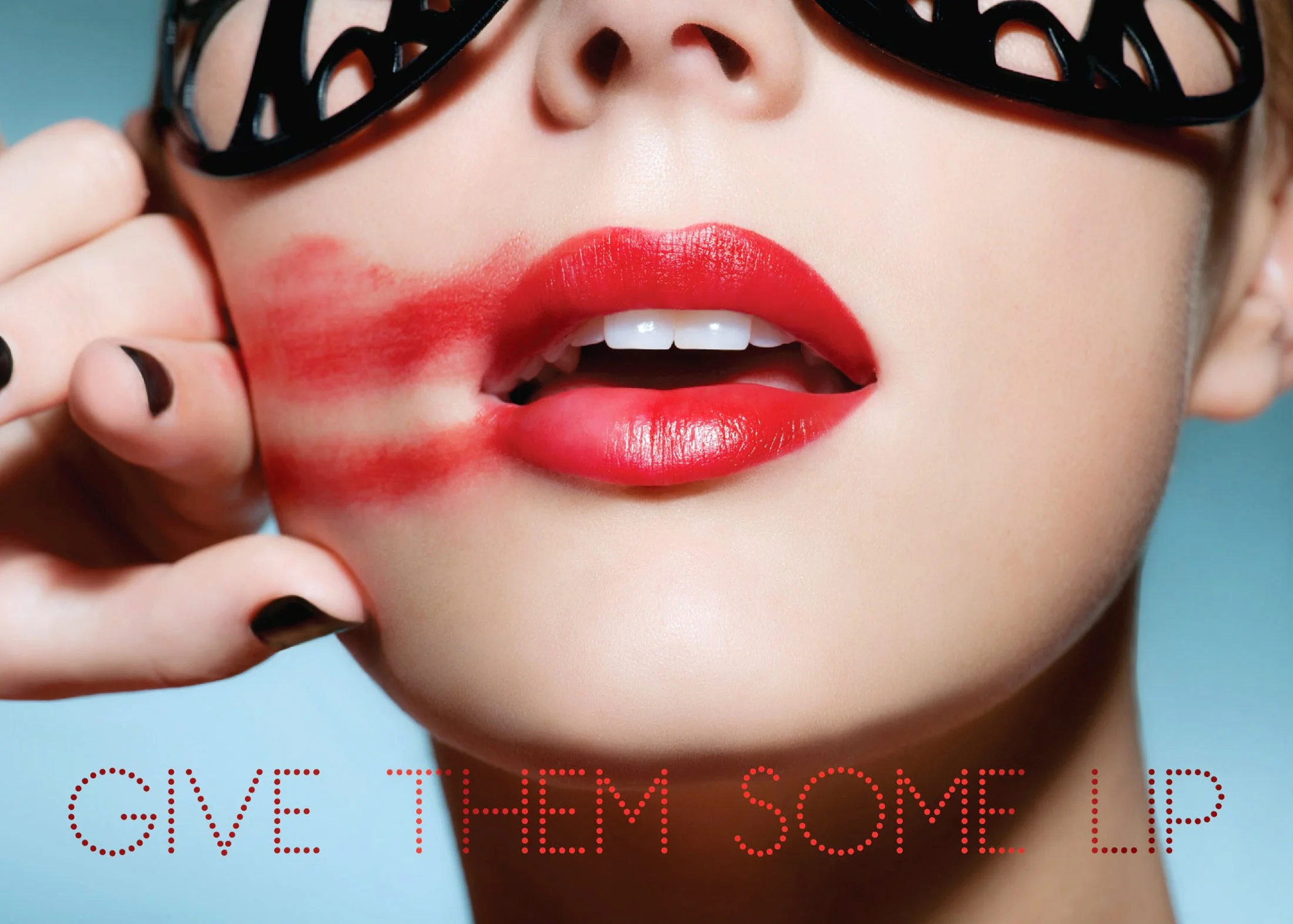 Close-up of a woman's face with red lipstick, black glasses, and finger touching her cheek, with red lipstick smudged on her face and the text 'GIVE THEM SOME LIP' at the bottom.