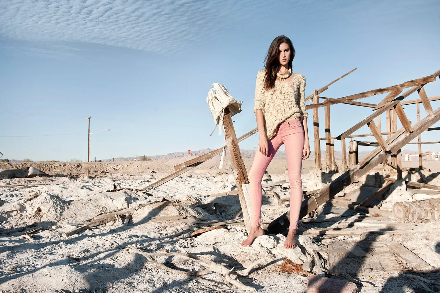 Ethereal desert fashion photography by Daniella Hehmann Photography for Eugene Jeans featuring a model in a textured cream sweater and pink denim trousers standing in the vast white salt flats of the Salton Sea.