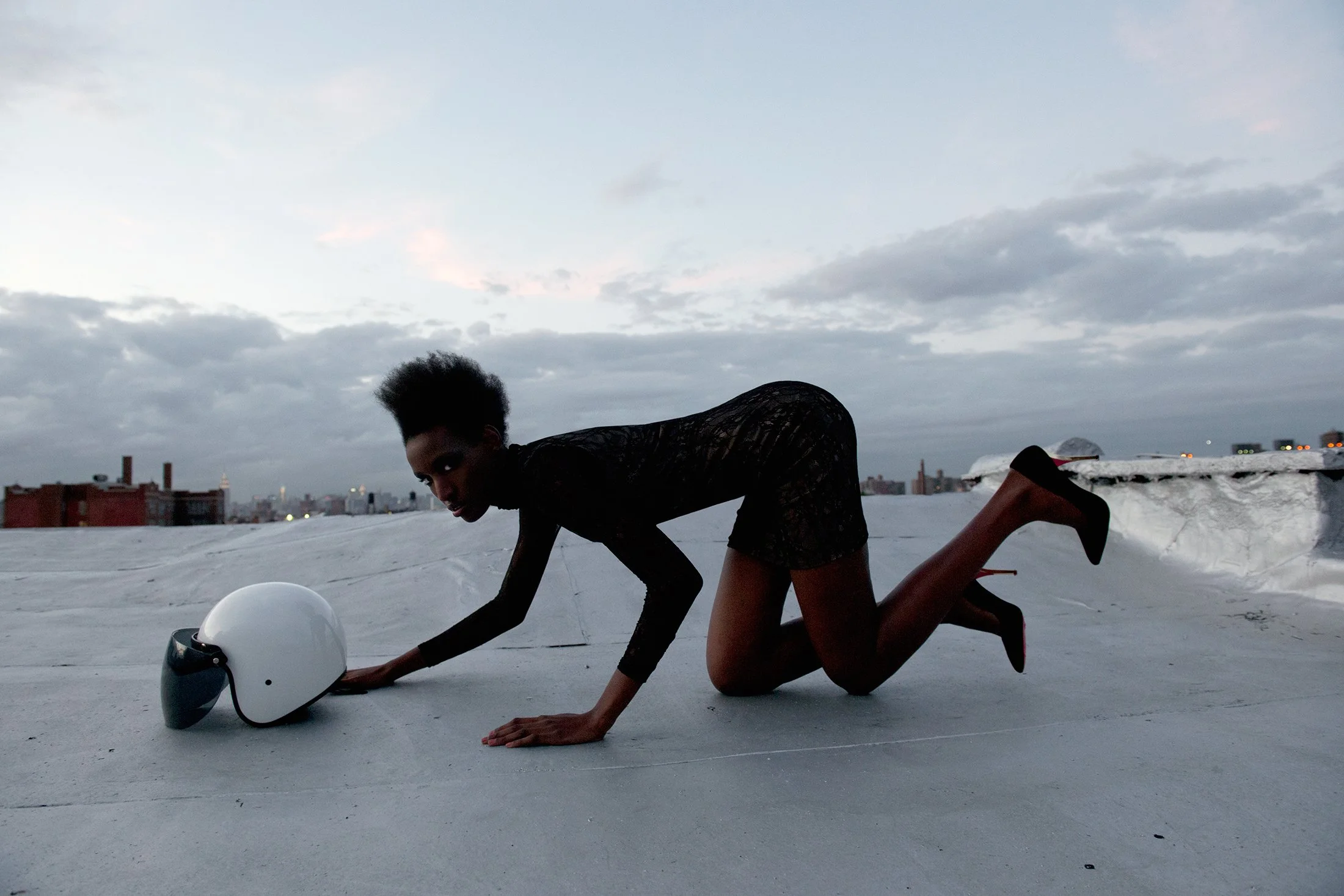 Cinematic fashion portrait by Daniella Hehmann Photography featuring model Kadiata Ba in a sleek black dress and heels, posing on a rooftop with the hazy Manhattan skyline and One World Trade Center in the background.
