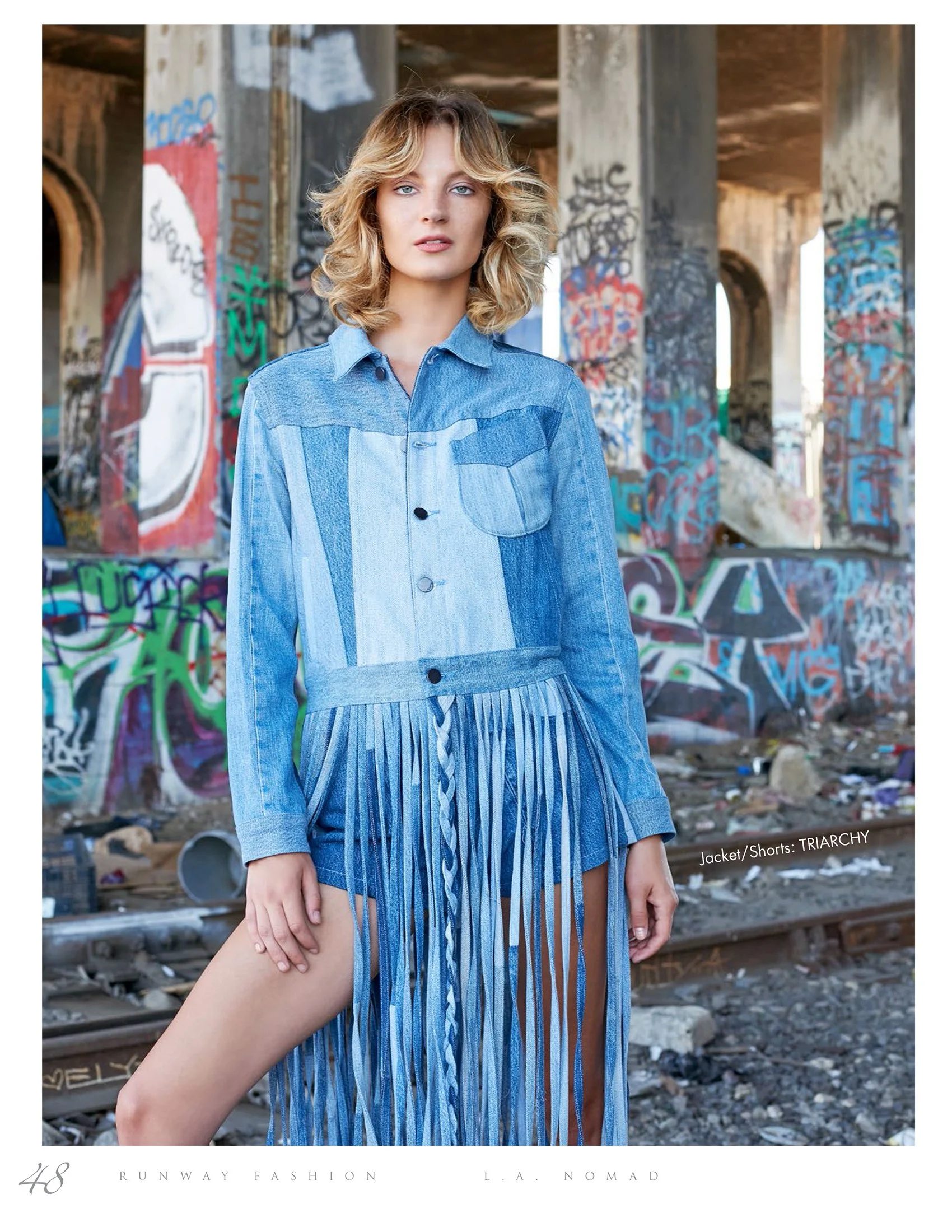 Edgy fashion photography by Daniella Hehmann Photography shot on location in L.A., featuring a model in a denim fringed outfit standing in front of vibrant urban graffiti and industrial ruins.