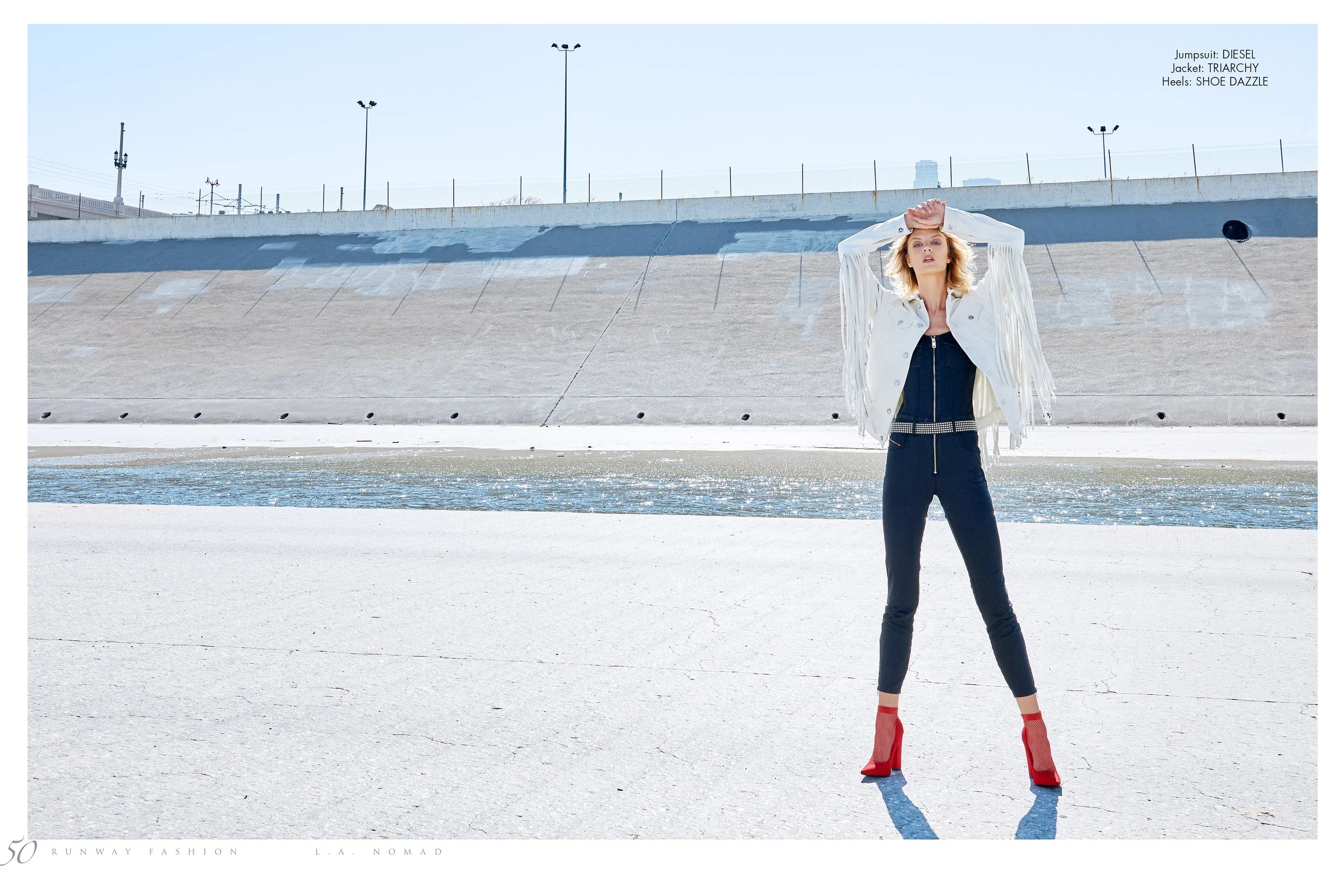 A wide-angle fashion shot by photographer Daniella Hehmann in the L.A. River basin. The model poses in a white fringed jacket and red boots, utilizing the stark, geometric lines of the Los Angeles urban landscape, shot in the L.A. riverbed.