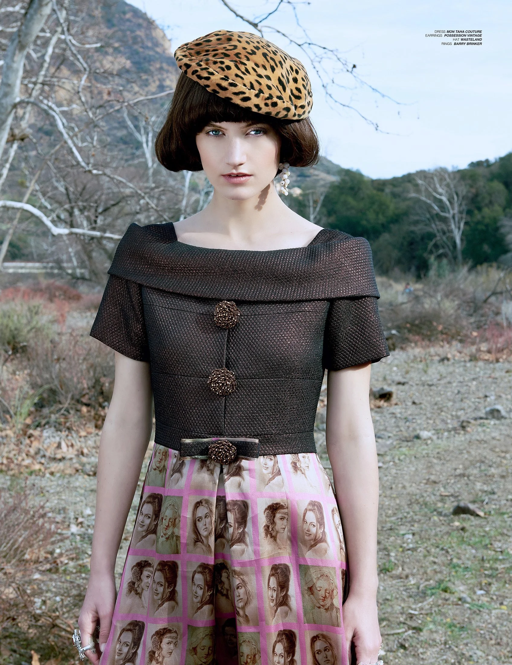 A sophisticated fashion portrait by Daniella Hehmann Photography in Los Angeles, featuring a model wearing a leopard print beret and a black textured top with decorative buttons, standing outdoors in a natural setting with trees and hills, during day