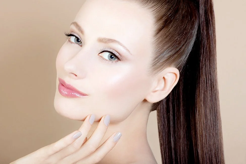 High-end cosmetic advertising for Senna Cosmetics by Los Angeles beauty photographer Daniella Hehmann, featuring artistry by Eugenia Weston. The model, styled with a high ponytail, displays a polished, luminous skin texture under soft, diffused beaut