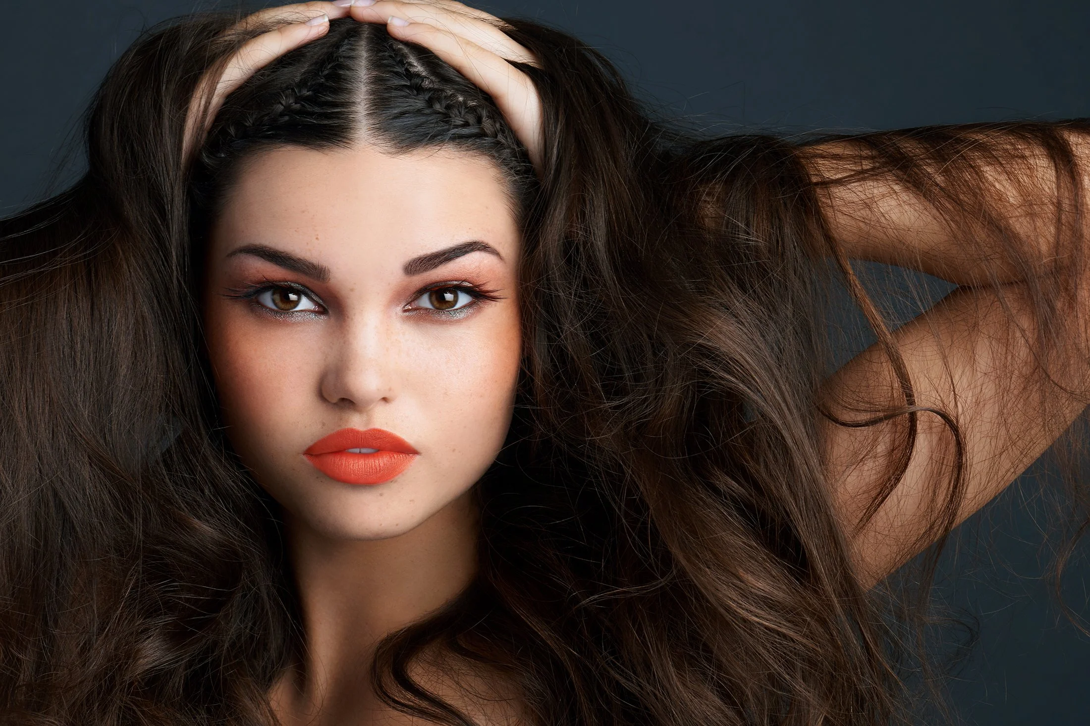 Editorial beauty photography for Senna Cosmetics Tribal Make-up series by Los Angeles beauty photographer Daniella Hehmann. Makeup by Eugenia Weston features bold, warm-toned eyeshadow and a vibrant orange-red lip. The lighting is focused and dramati