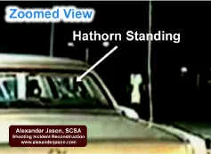 Hawthorn has exited his vehicle and is standing at the open door. Out of view on the left, the suspect points/aims his cell phone.