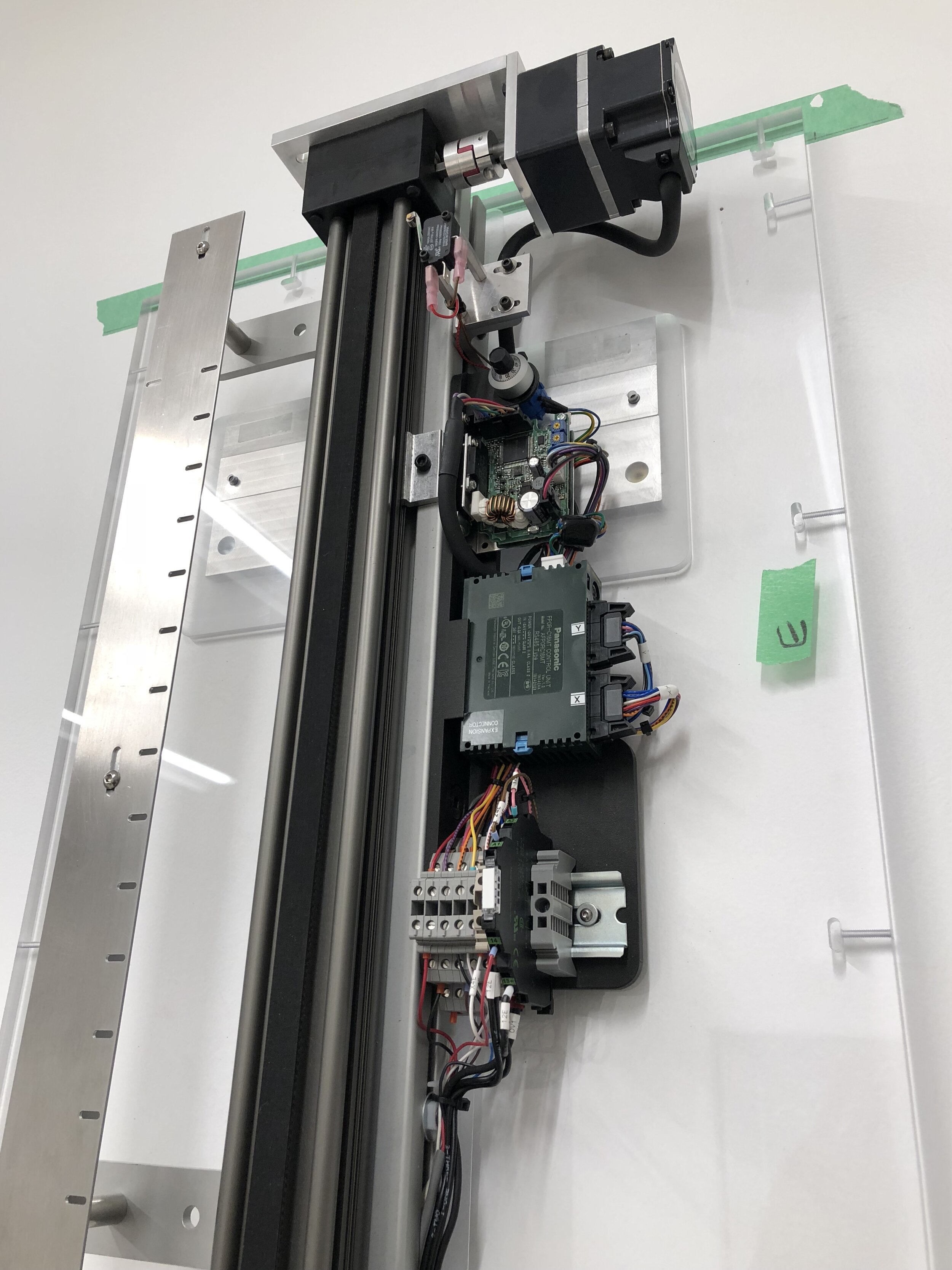  Detail,   electrical hardware, motor, motor driver, programmable logic controller (PLC) and wiring. Optical sensor slots  are visible on the left. Each slot corresponds to the vertical position of  a single word engraved in the acrylic.     