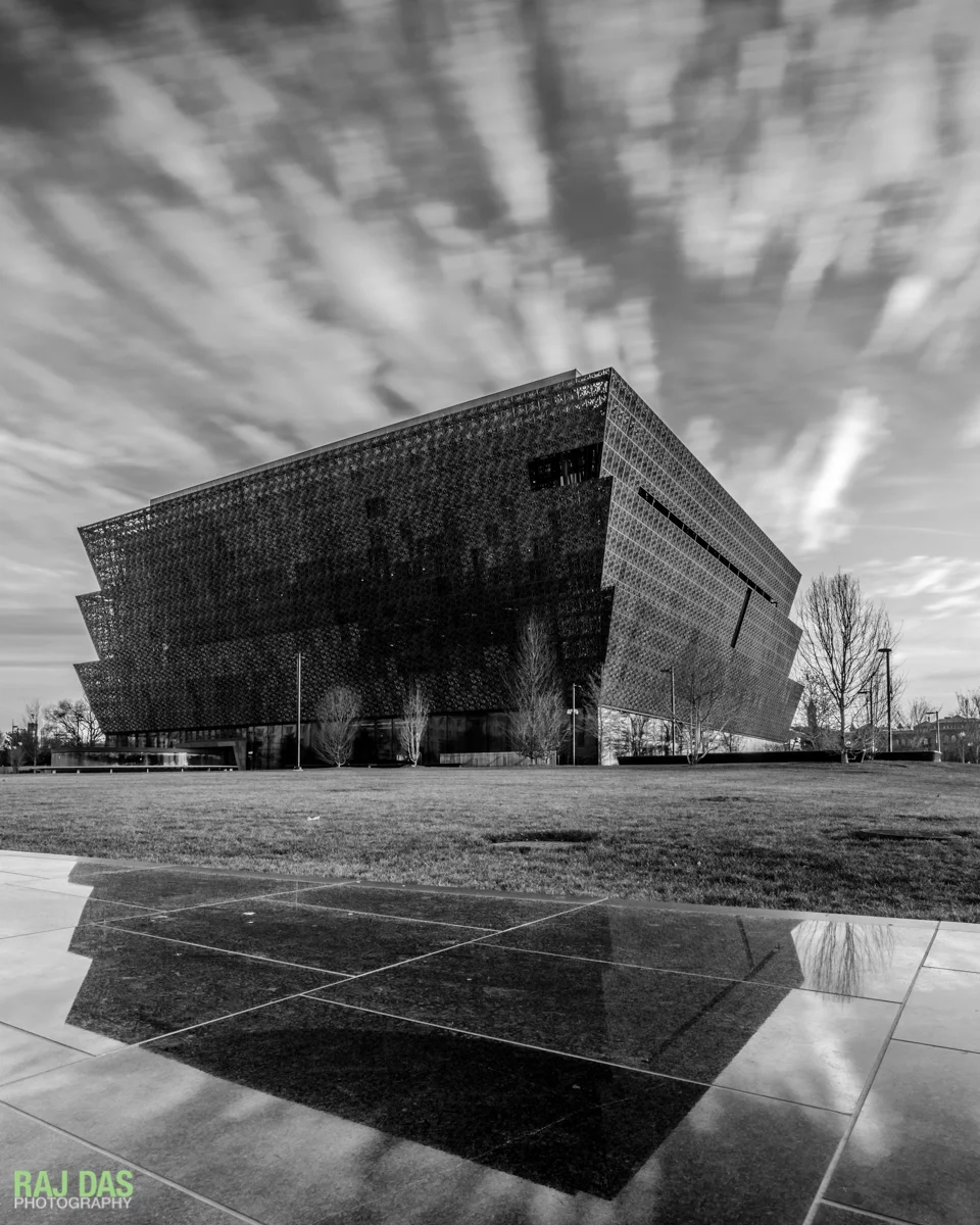 The Museum and clouds reflected on the black granite retaining wall along Constitution Avenue