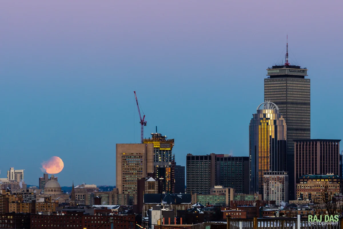 A super blue blood moon sets just as the sun rises in the opposite direction casting a warm glow over the Boston skyline.