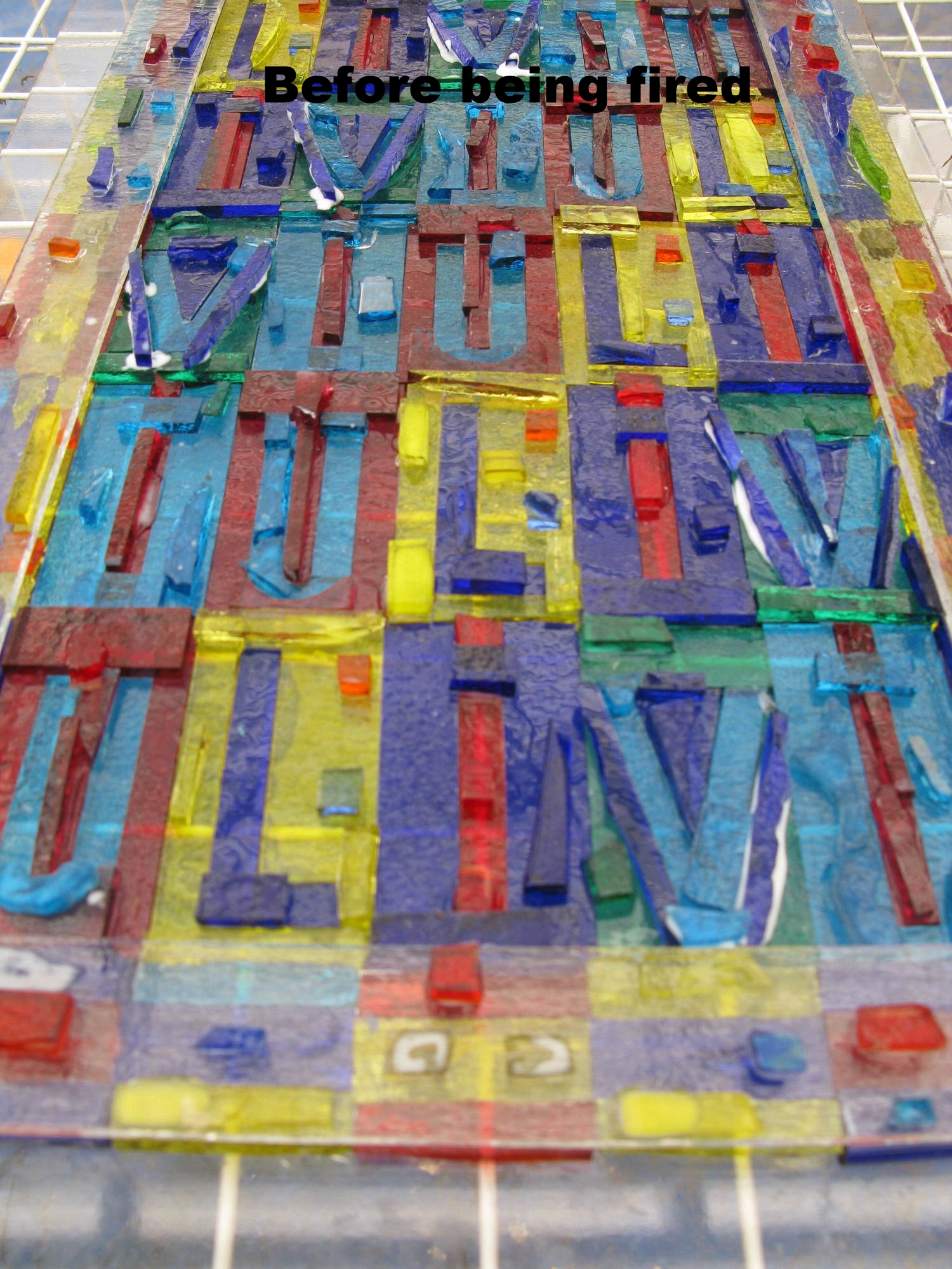  Play on the letters 'Liviu,' which are rotated around. &nbsp;The glass before being fired. &nbsp; You would not want to leave the glass as is because it would not permanently adhere to the base white glass it is on.  2010  Fused glass. 