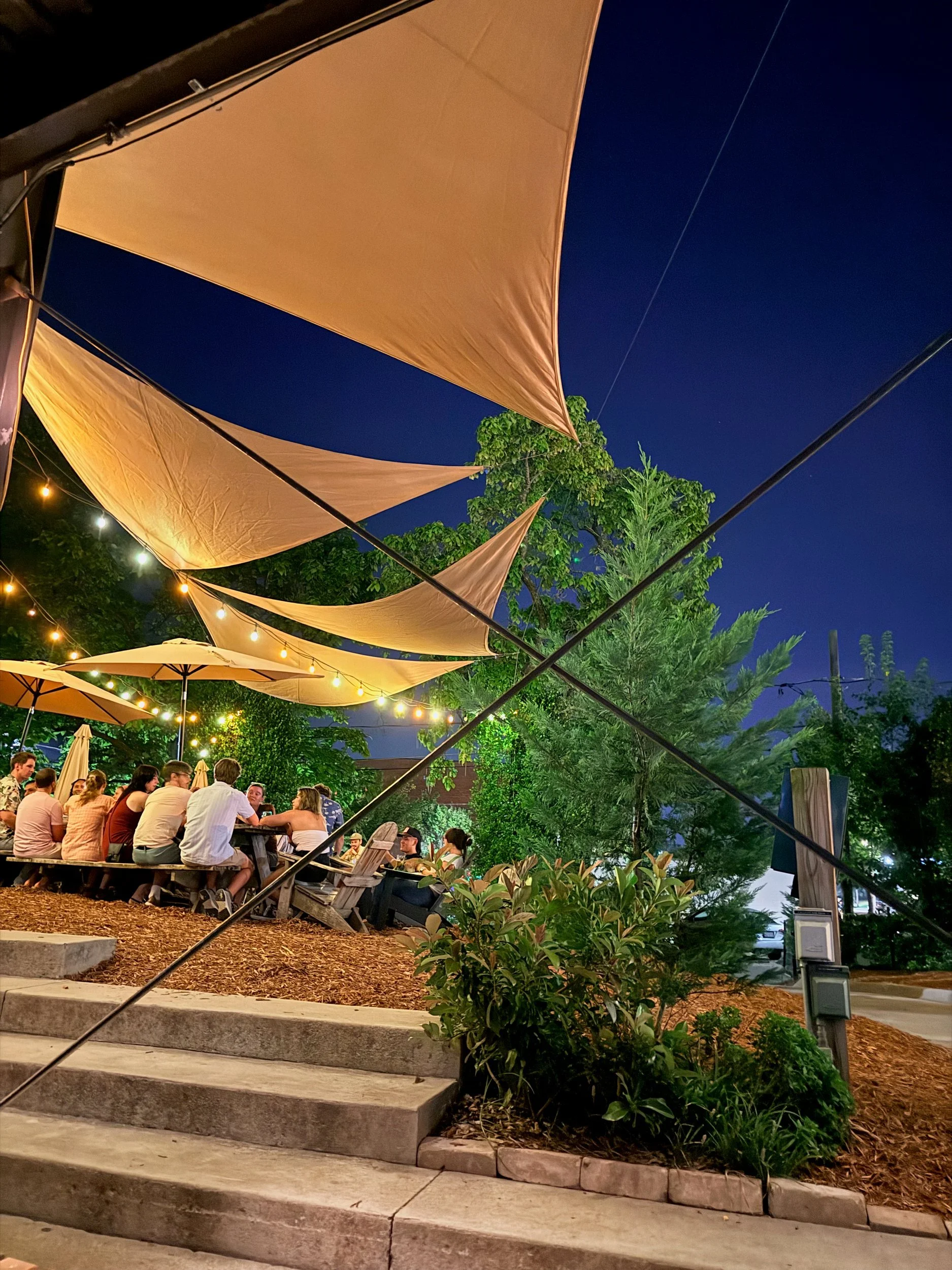 Outdoor patio at night under glowing sail shades and string lights