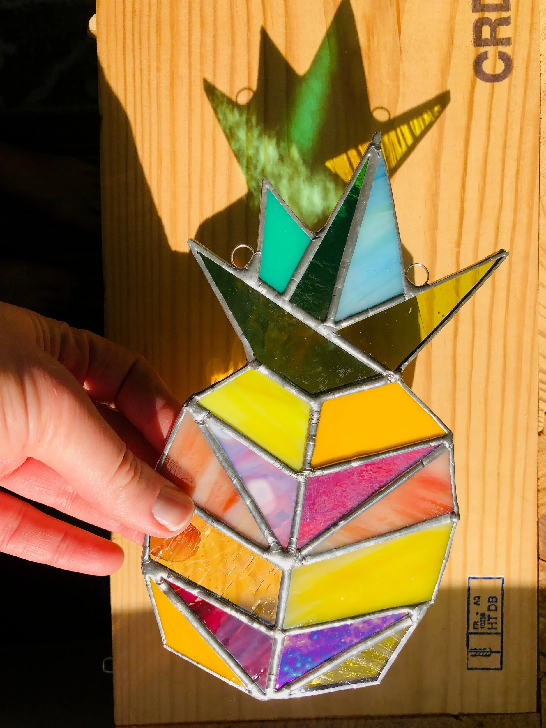 Stained glass pineapple by Angela Martin Kobrick casting colored light on wood