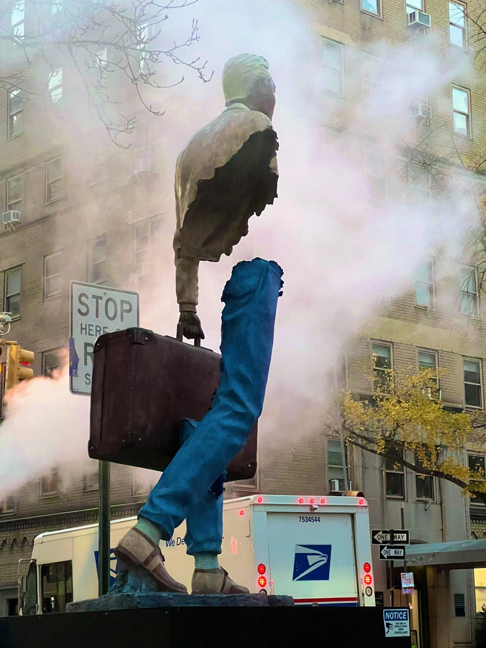 Sculpture of a walking figure with a suitcase in street steam, New York City