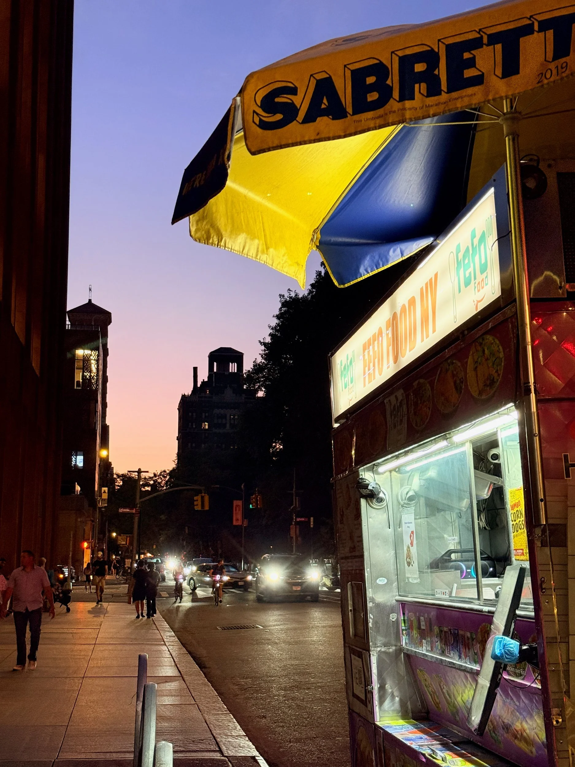 Sabrett hot dog cart glowing at dusk on a New York City street