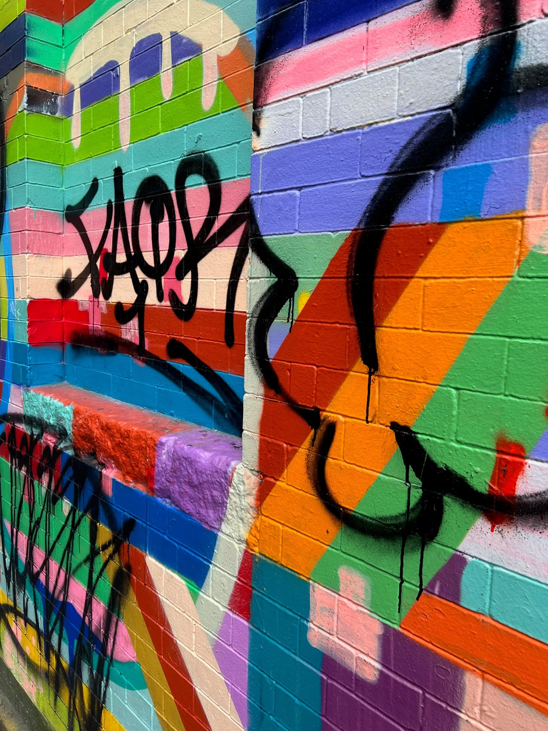 Graffiti over a brightly painted geometric wall