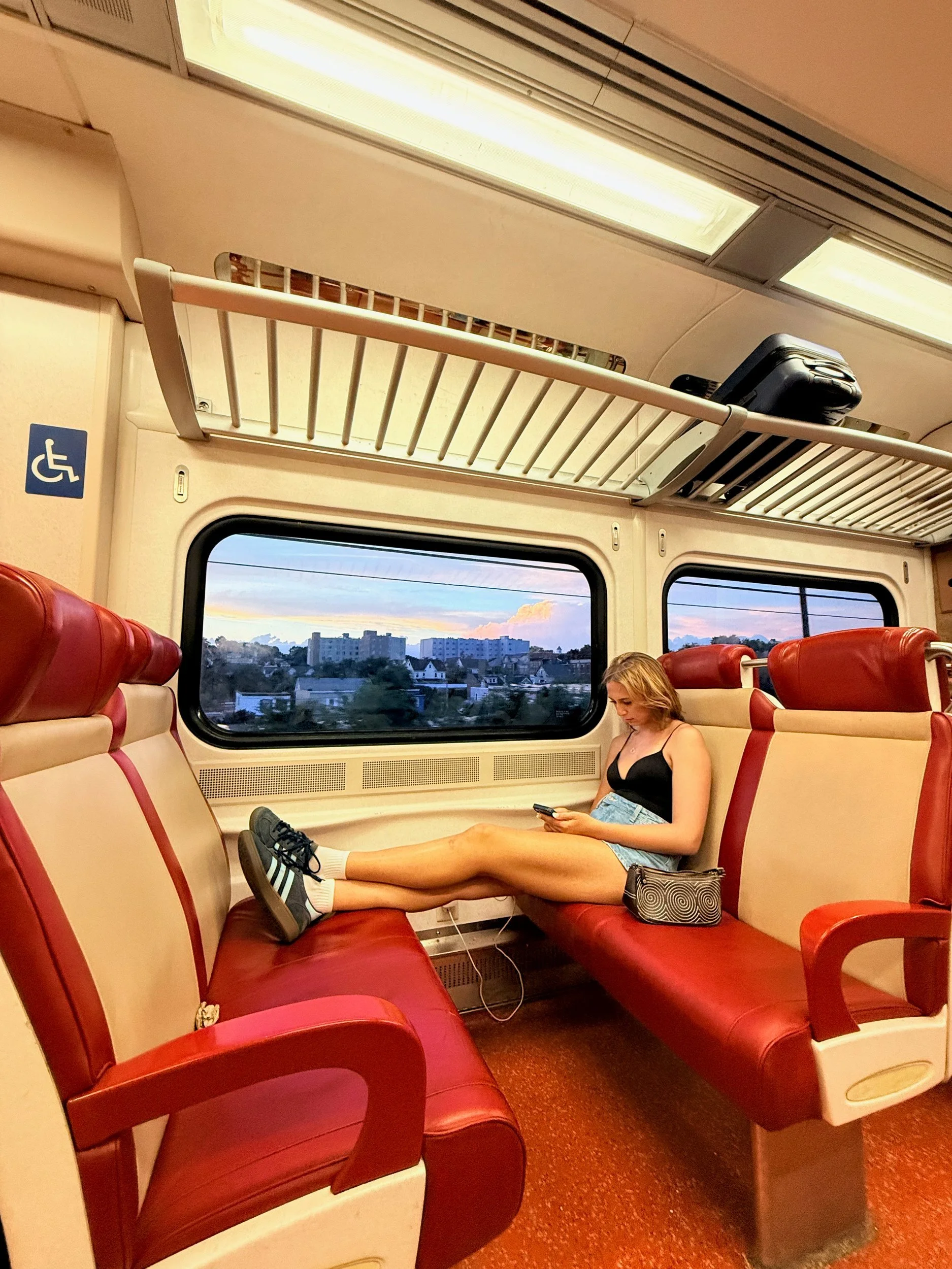 Commuter train car with red seats, a passenger stretched out by the window