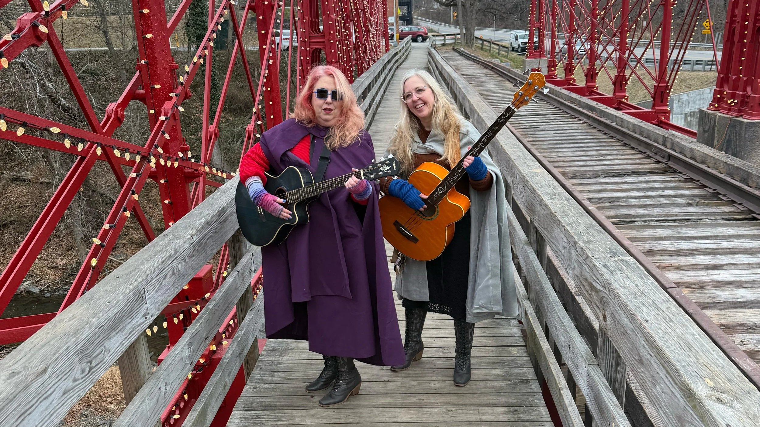 two women standing on a bridge holding guitars.