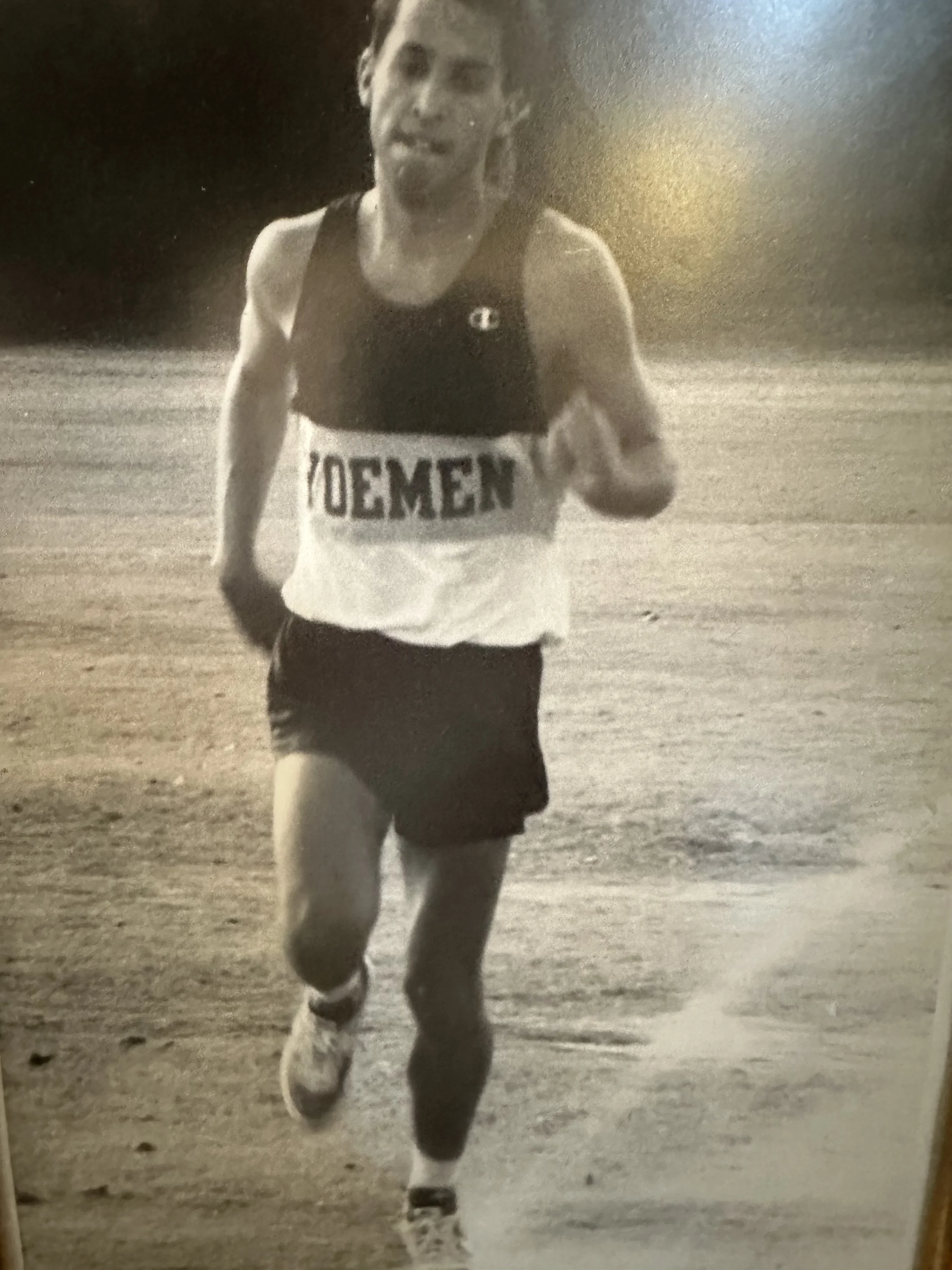 A black and white photograph of a man running on a dirt or gravel path.