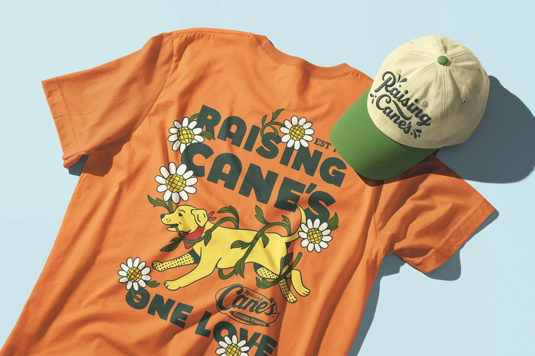 Raising Cane’s orange graphic T-shirt with yellow Labrador illustration and green baseball cap