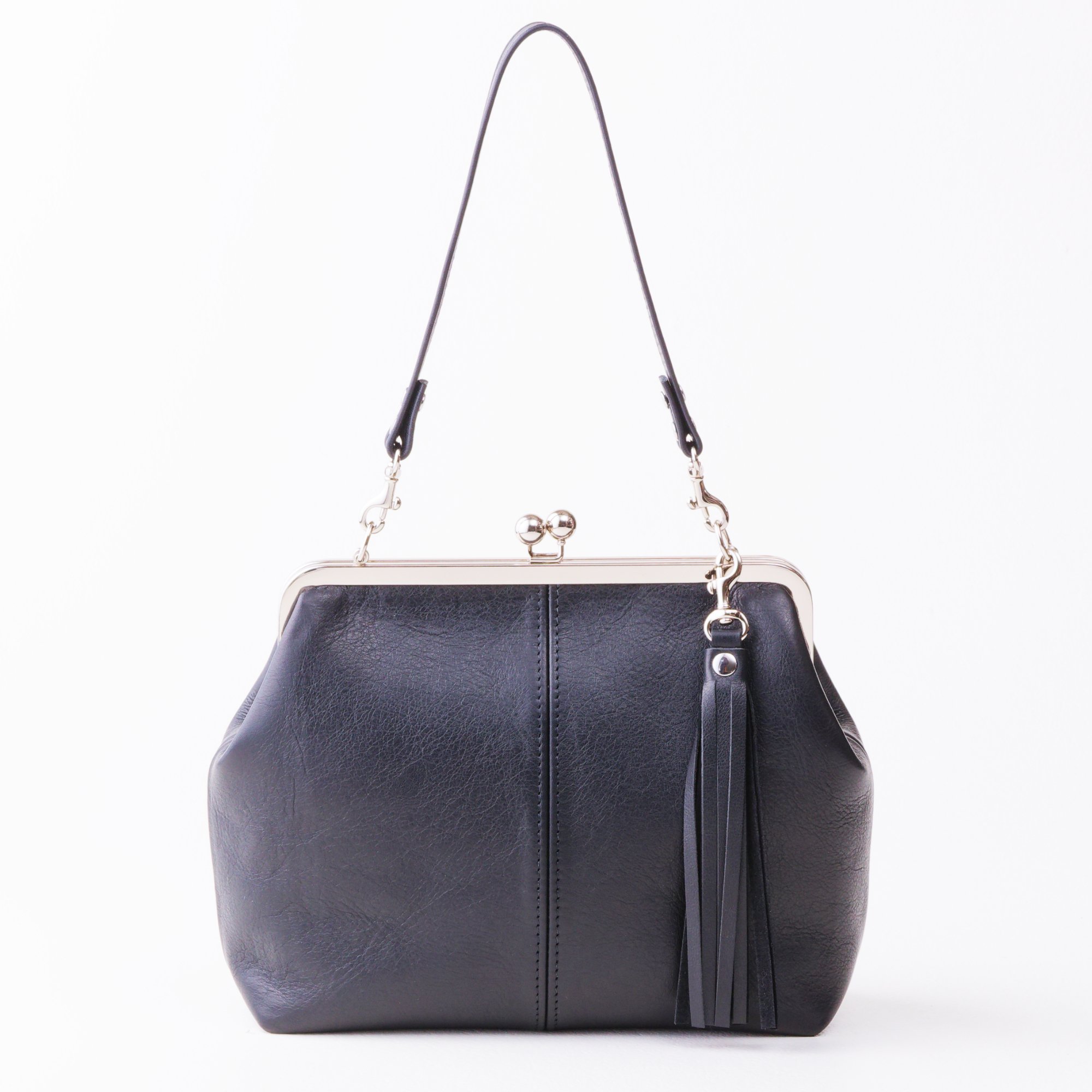 Front view of black leather kiss lock handbag with silver finish hardware, shorty shoulder strap and tassel charm on tabletop.