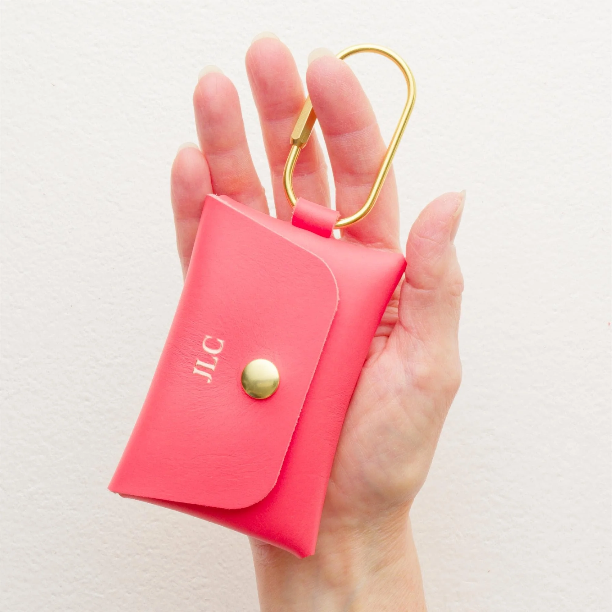 Hand holding personalized coral color leather carabiner keychain wallet / purse charm with gold finish hardware and rose gold foil monogram.