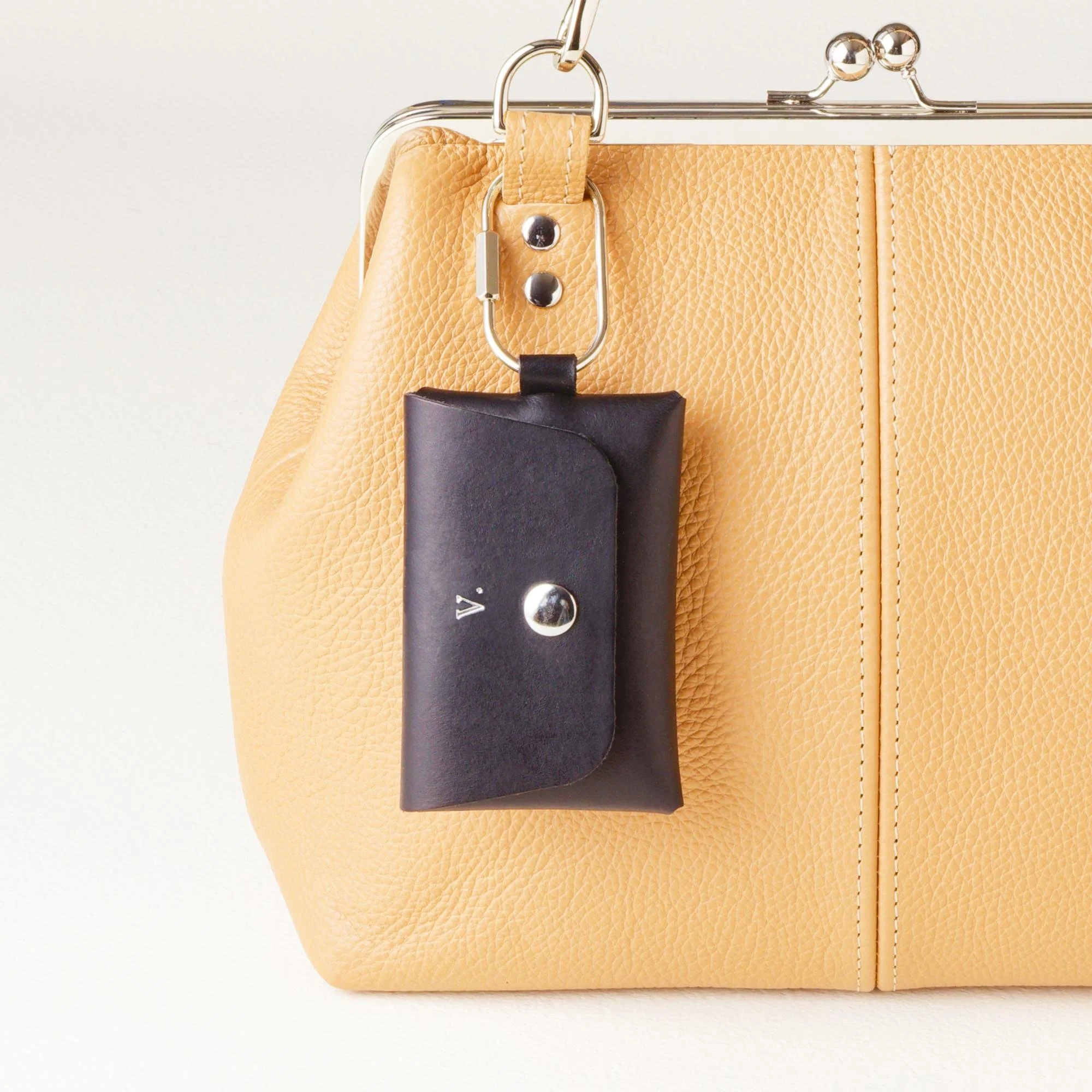 Personalized black leather carabiner keychain wallet / purse charm with silver finish hardware and silver monogram initial, attached to tan leather kiss lock handbag strap.