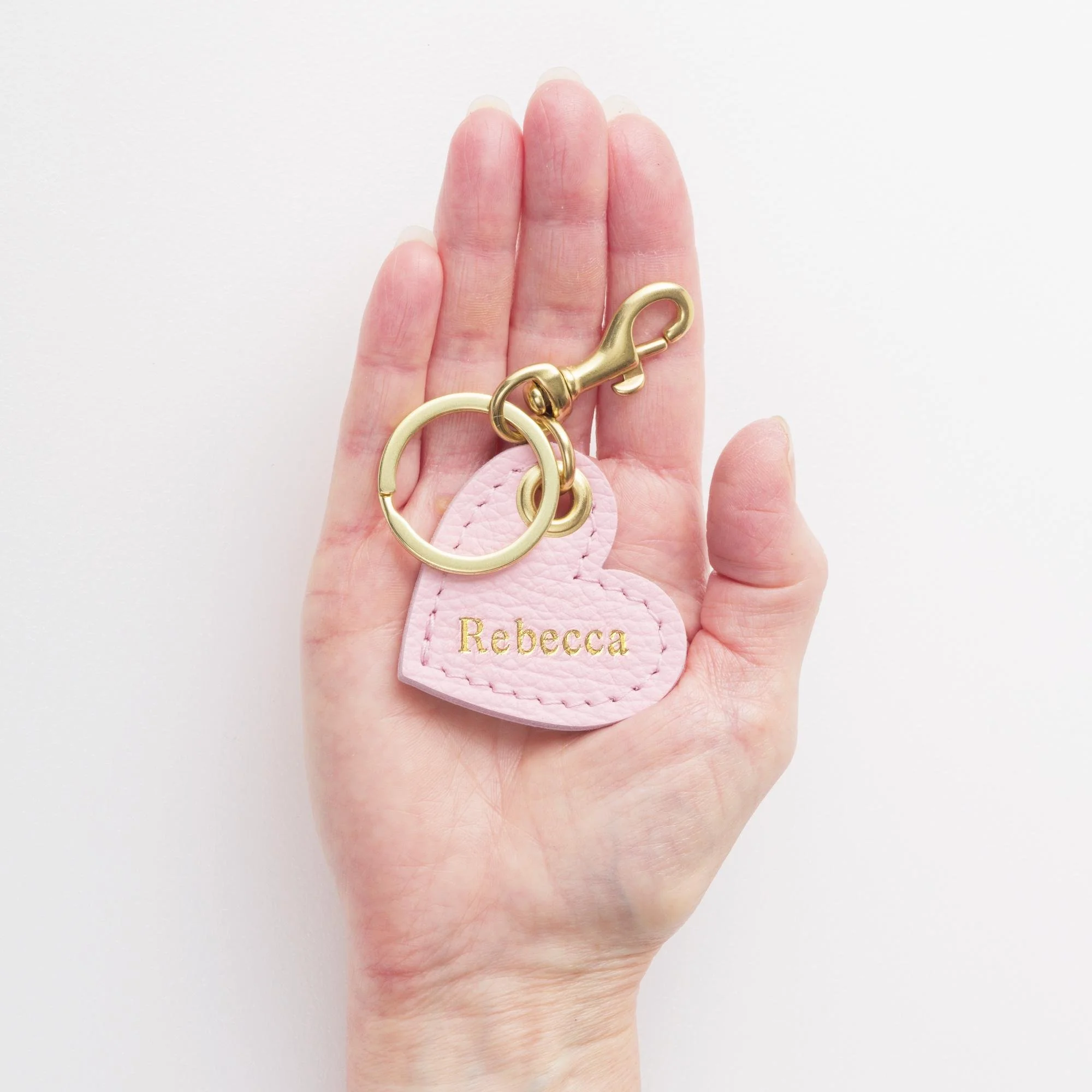 Hand holding personalized pink leather keychain with gold finish hardware.