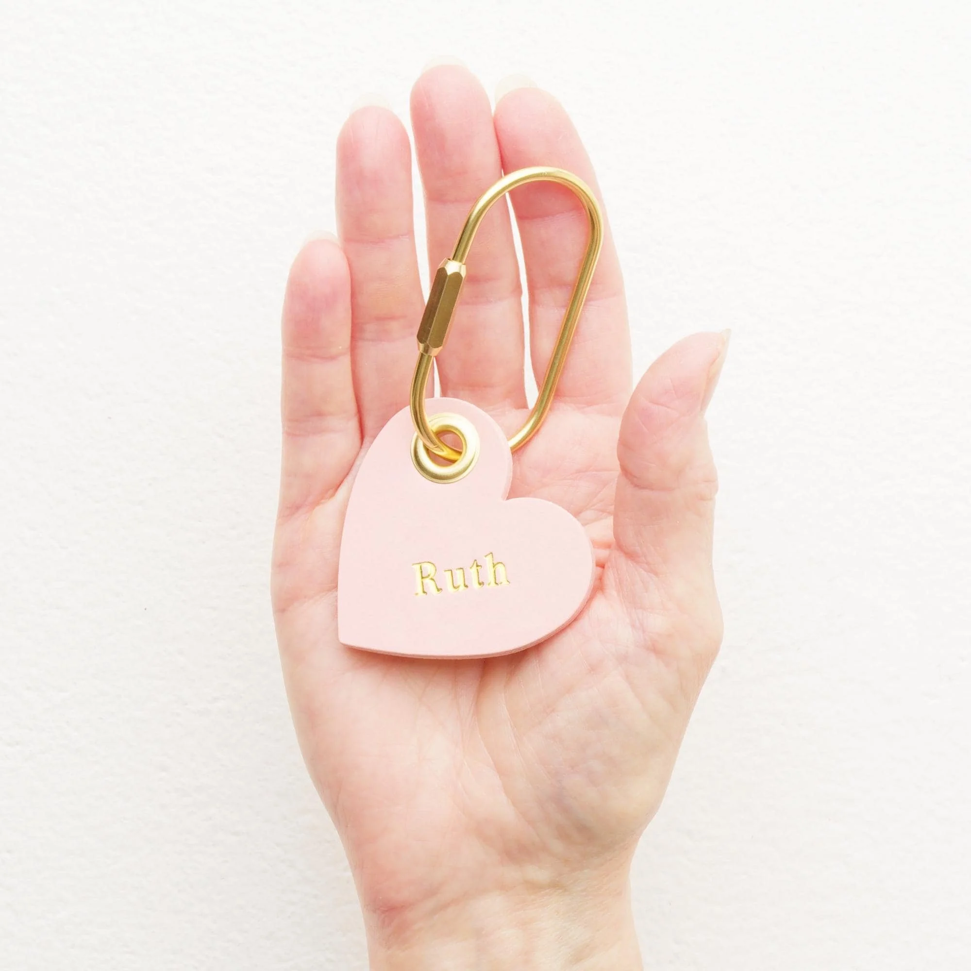 Hand holding personalized pink heart shaped leather carabiner keychain / purse charm with gold hardware.