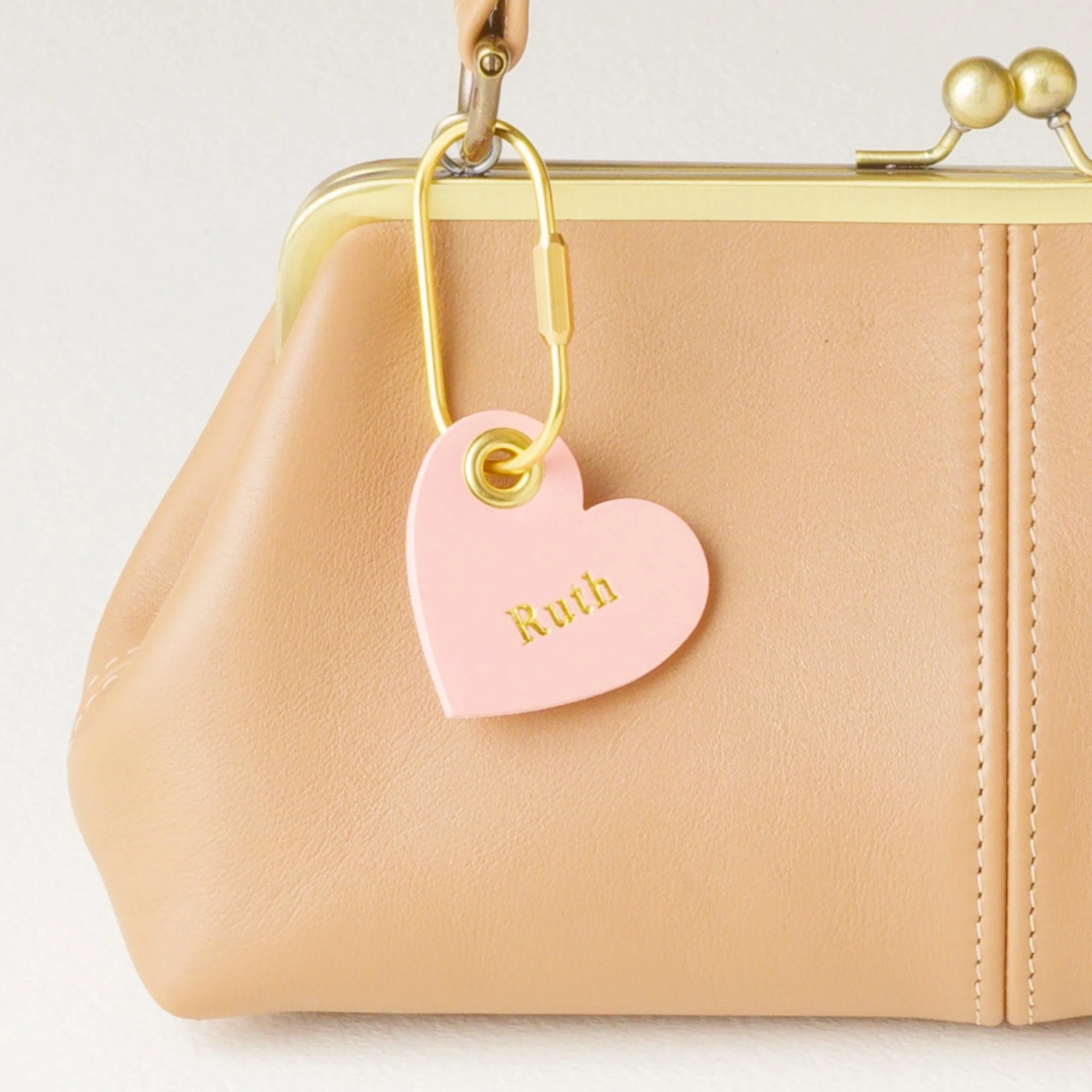 Personalized pink heart shaped leather purse charm / keychain with gold finish hardware attached to kiss lock handbag.