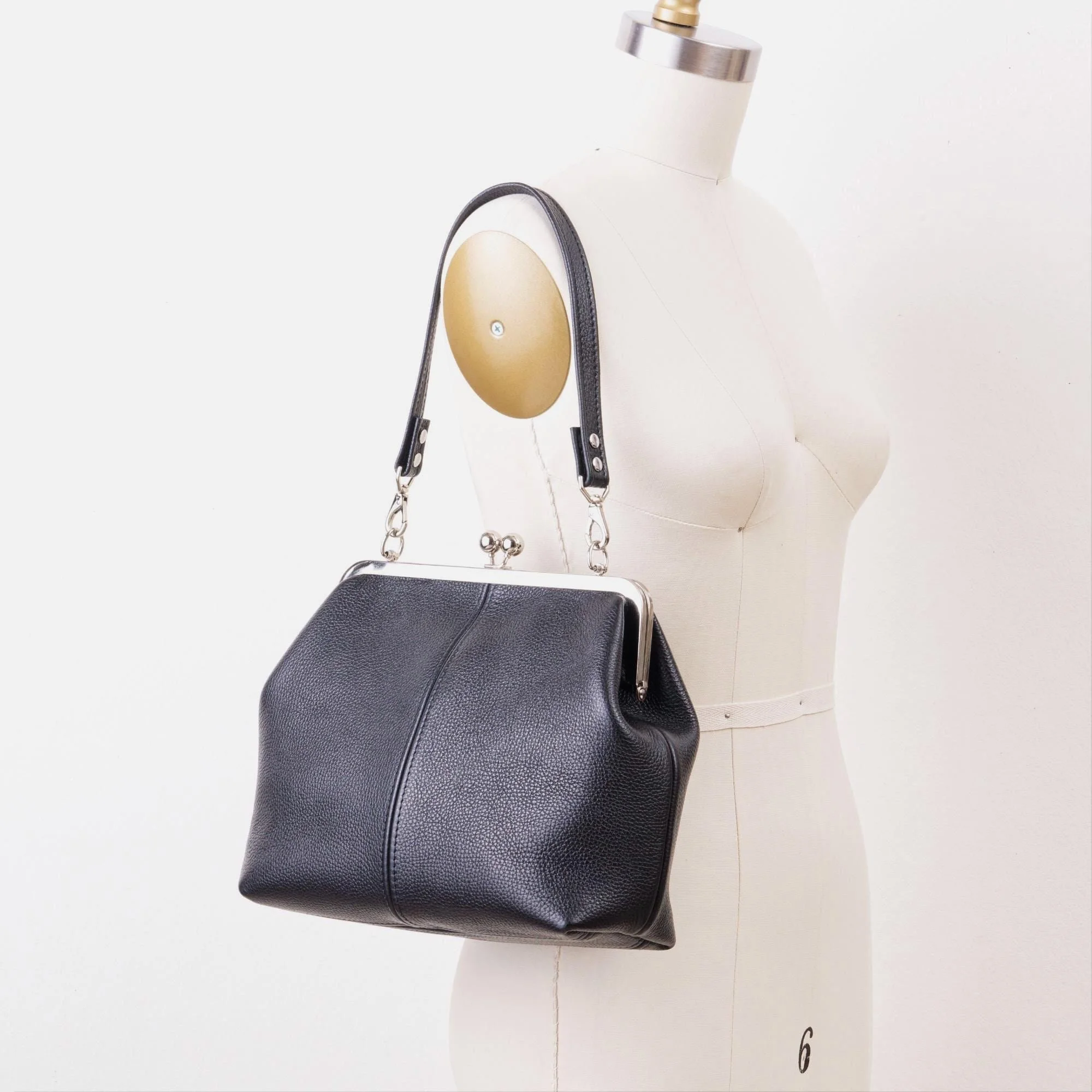 Black pebble grain leather kiss lock handbag with silver finish hardware and shorty shoulder strap on mannequin.