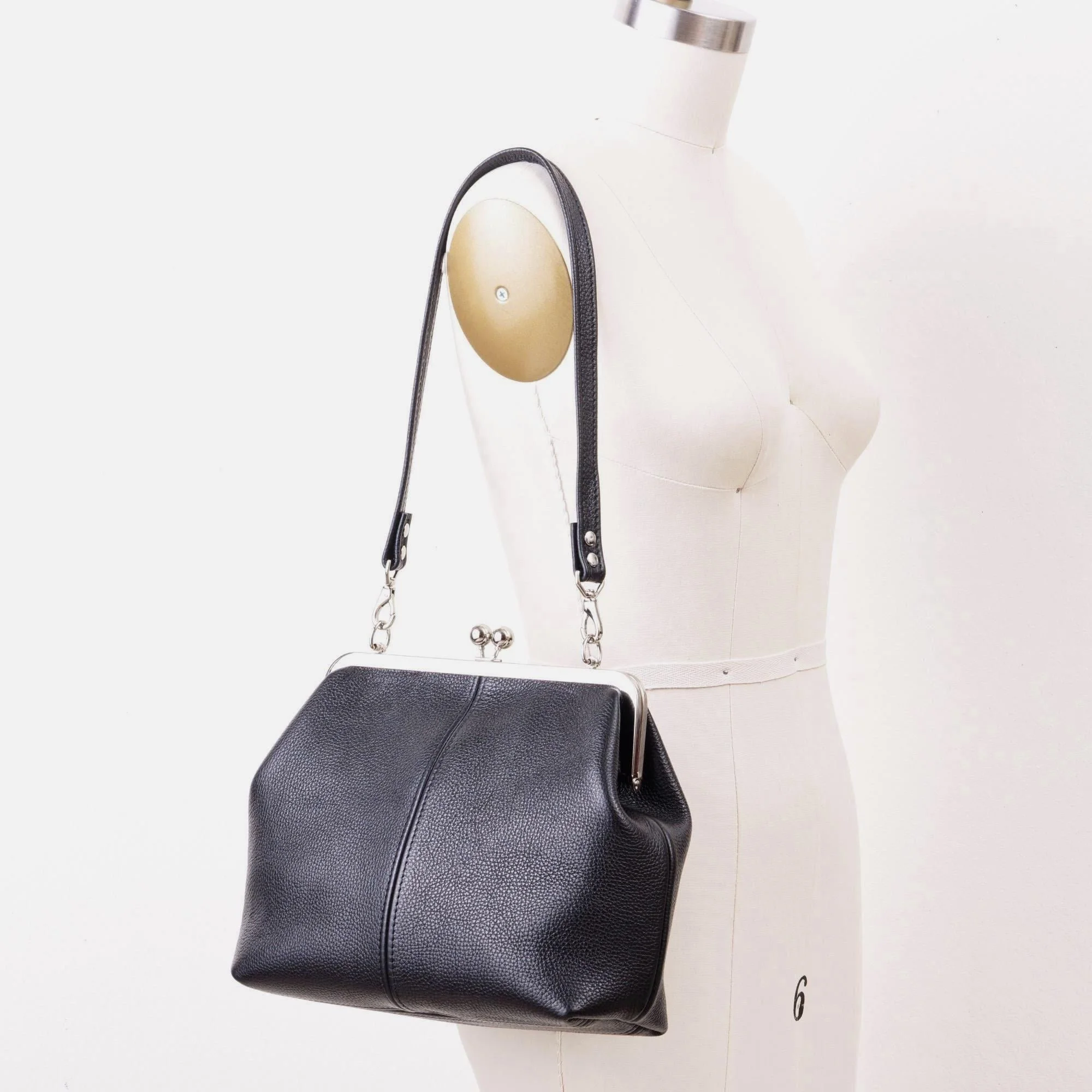 Black pebble grain leather kiss lock handbag with silver finish hardware and standard shoulder strap on mannequin.