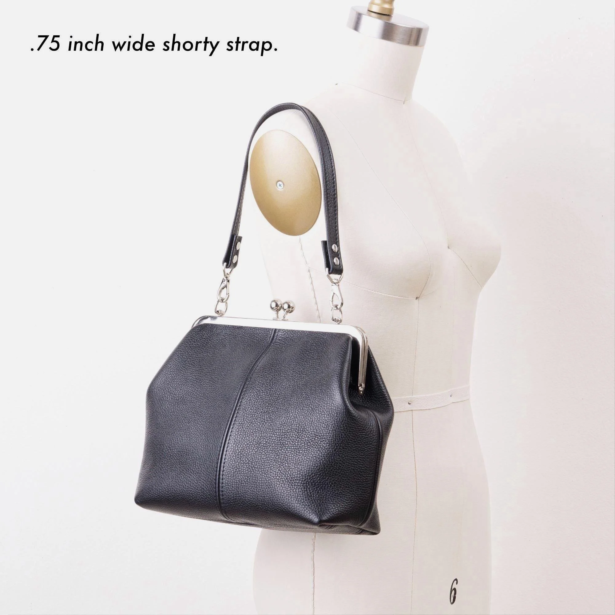 Black pebble grain leather kiss lock handbag with silver finish hardware and shorty shoulder strap on mannequin with strap description.