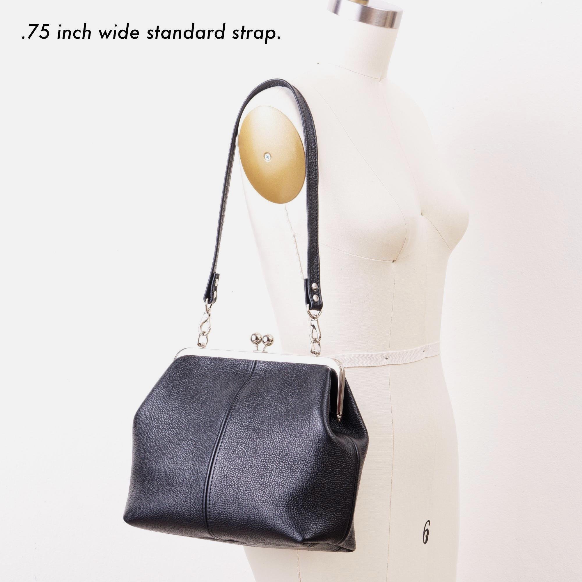 Black pebble grain leather kiss lock handbag with silver finish hardware and standard shoulder strap on mannequin with strap description.