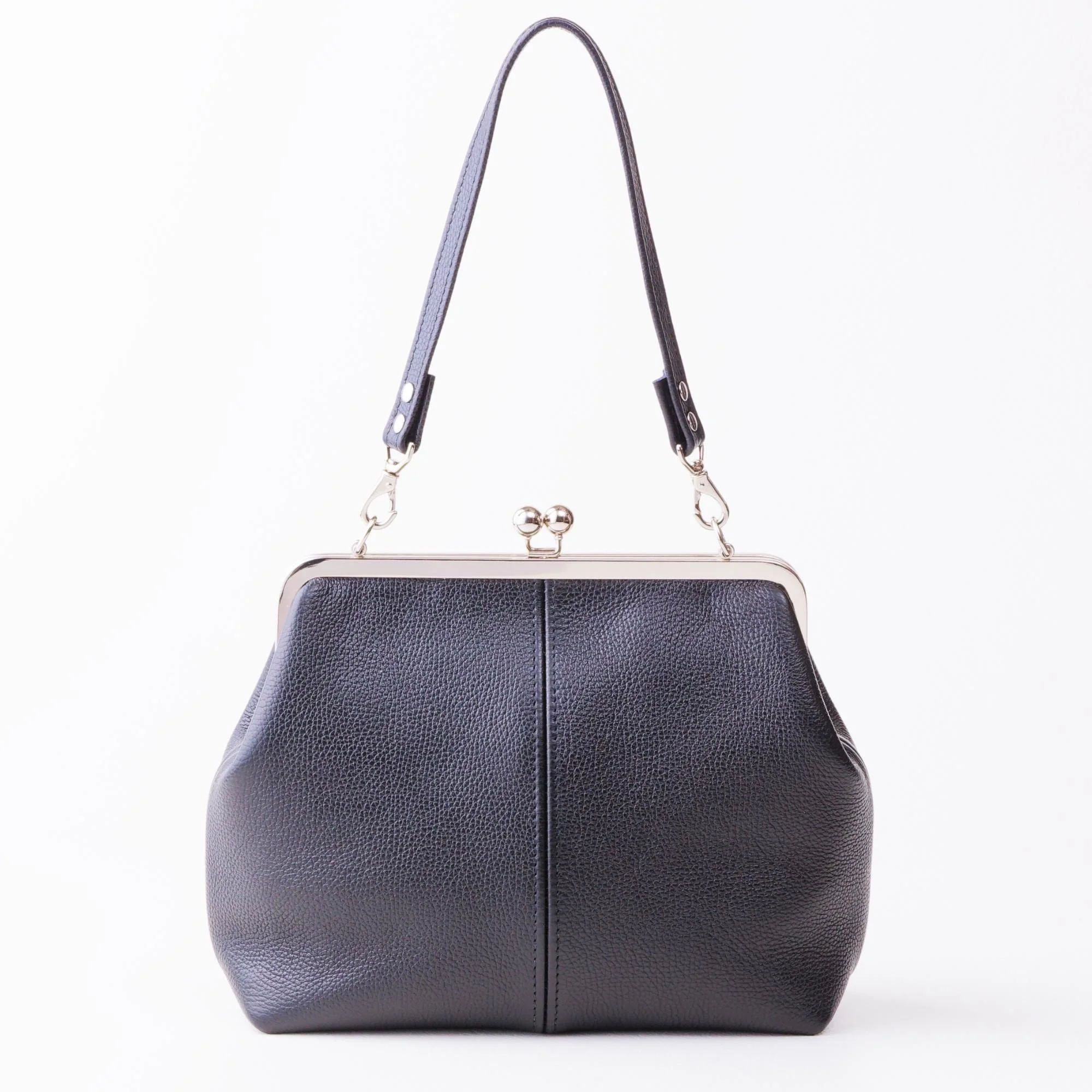 Front view of black pebble grain leather kiss lock handbag with silver finish hardware and shorty shoulder strap on tabletop.