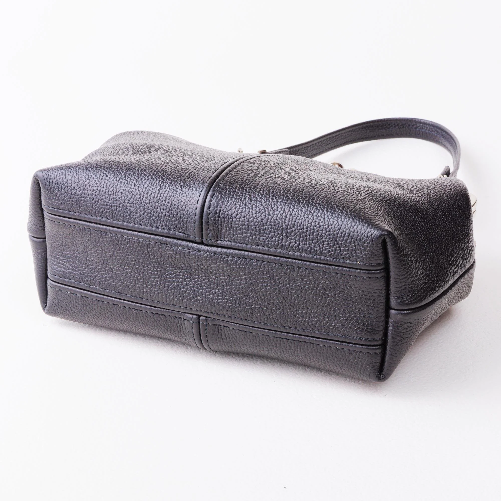 Bottom view of black pebble grain leather kiss lock handbag on tabletop.