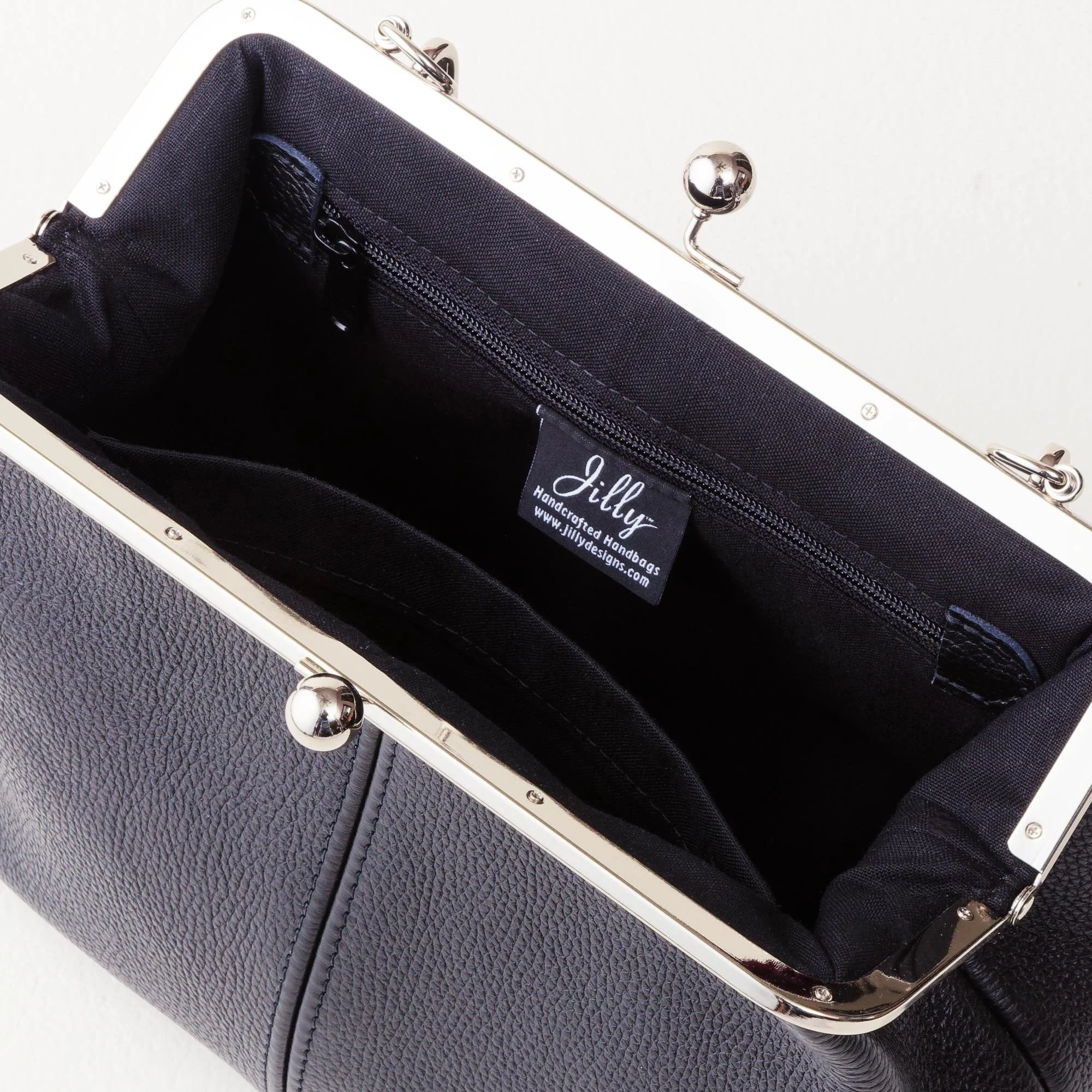 Interior view of black pebble grain leather kiss lock handbag with silver finish hardware, zipper pocket and slip pocket.